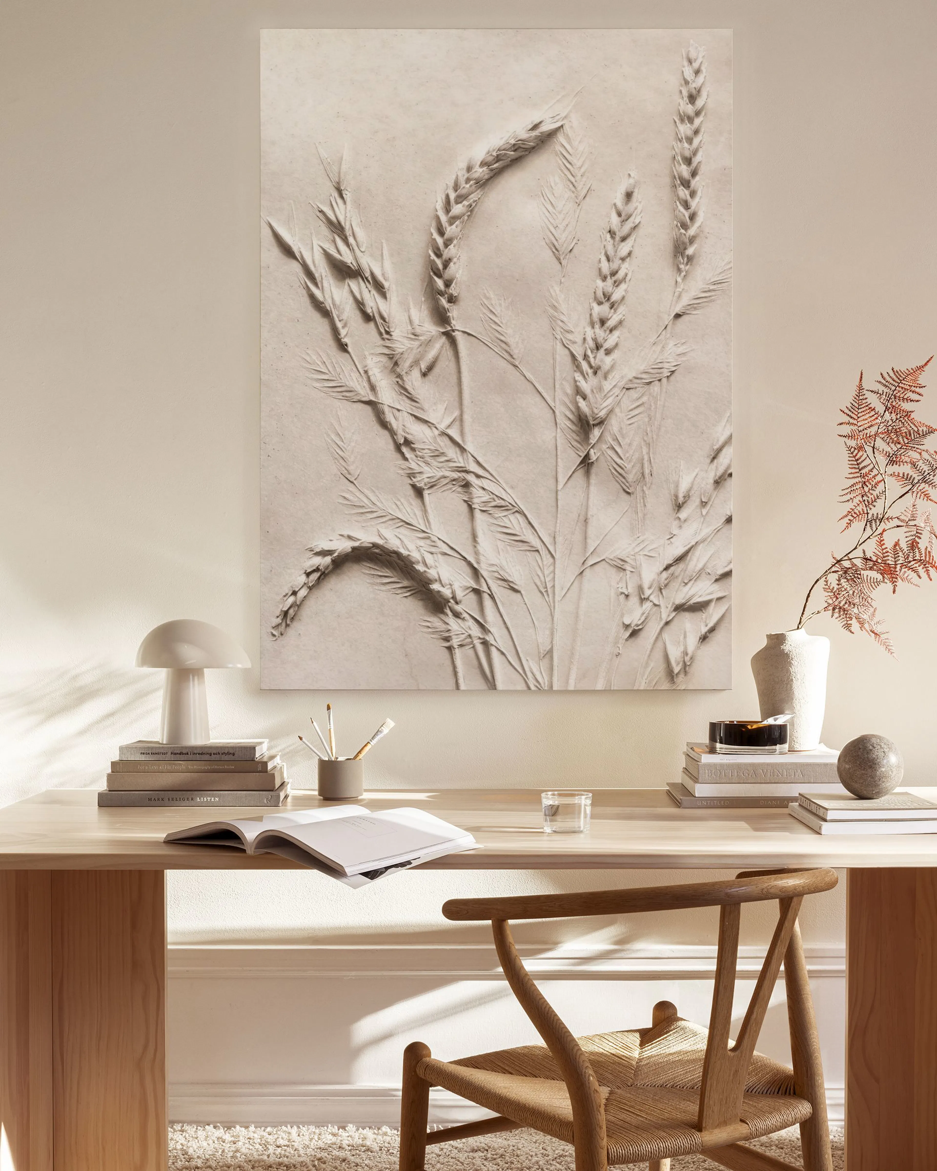Beige Leinwandbild mit reliefartigen Ährenmotiven, hängend über einem Sideboard in einem hellen Wohnzimmer.