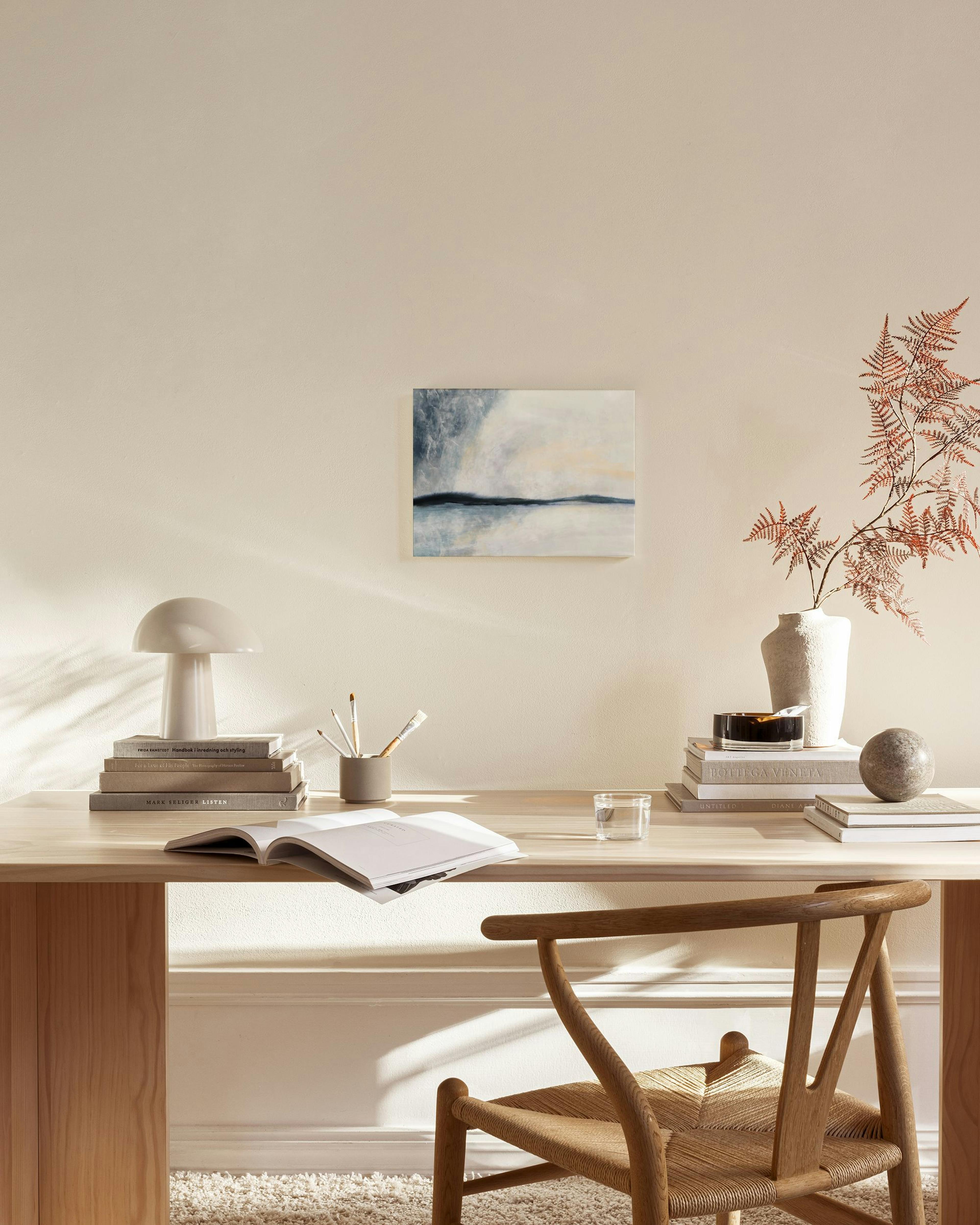 Lærred med abstrakt landskab i blå, grå og beige nuancer, hængende i en stue over et træmøbel.