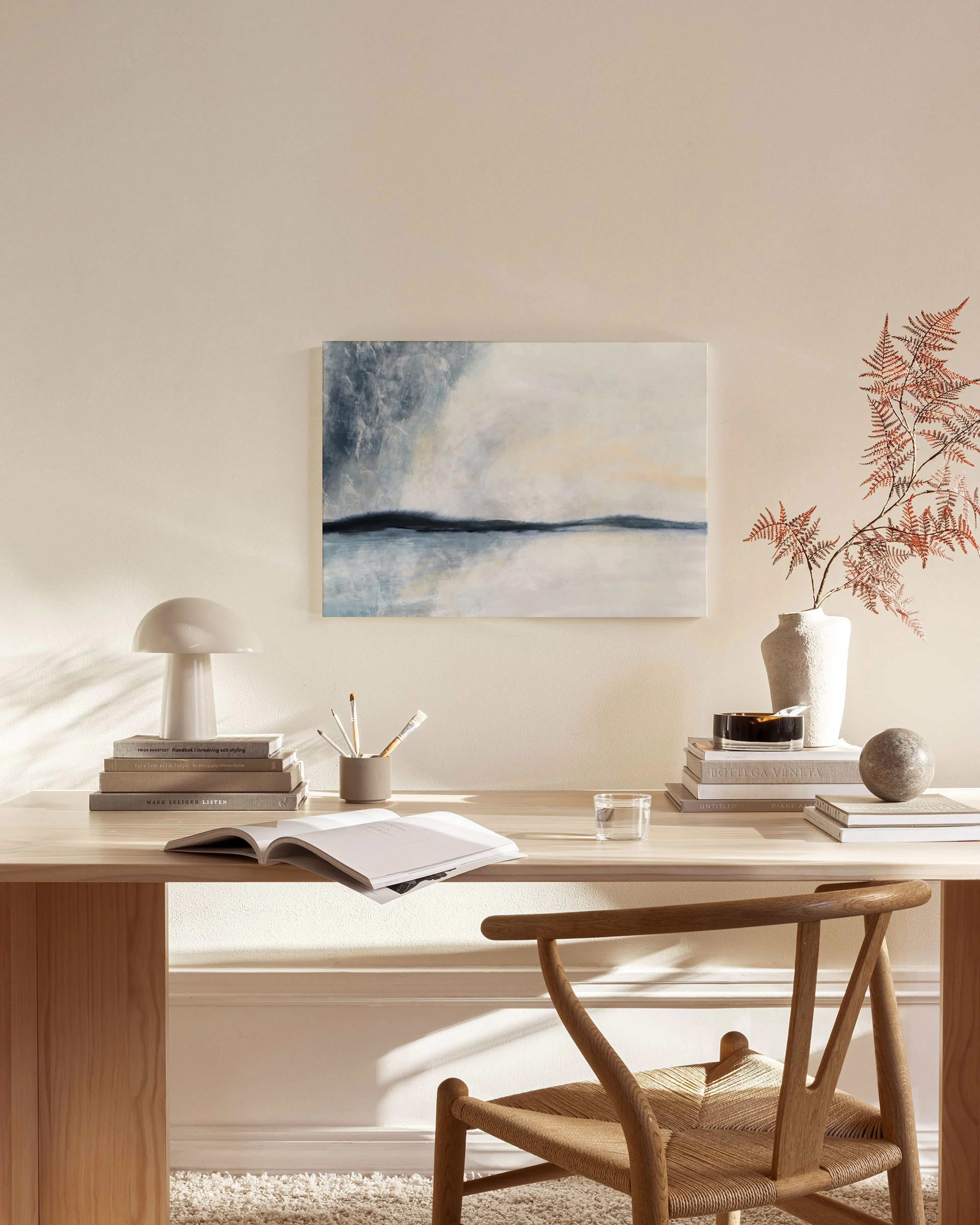 A serene landscape canvas in blues and creams, hanging above a console table in a minimalist living room.