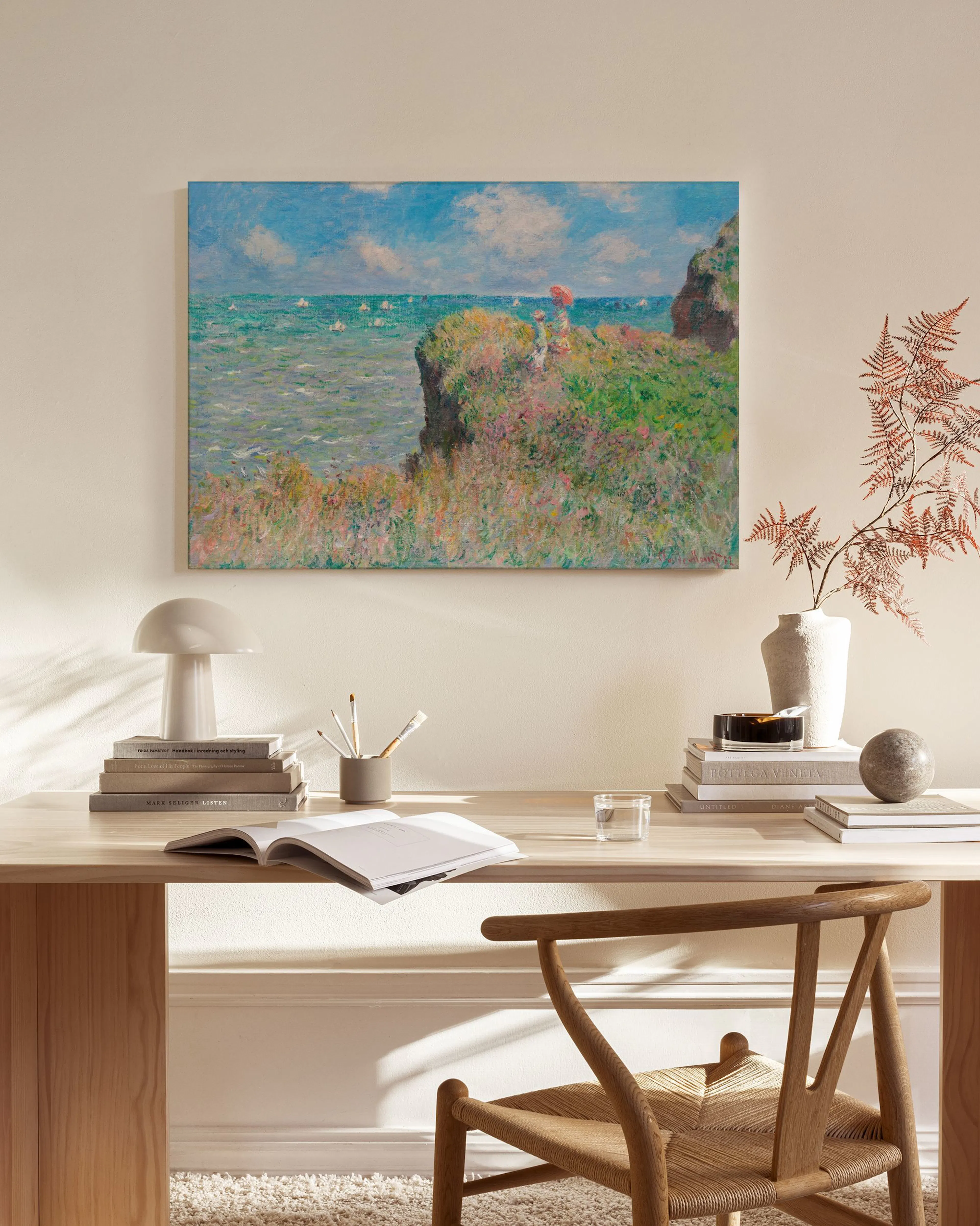 Canvastavla med Monet-målning av klippor vid havet, hängande ovanför en bänk i ett ljust vardagsrum.