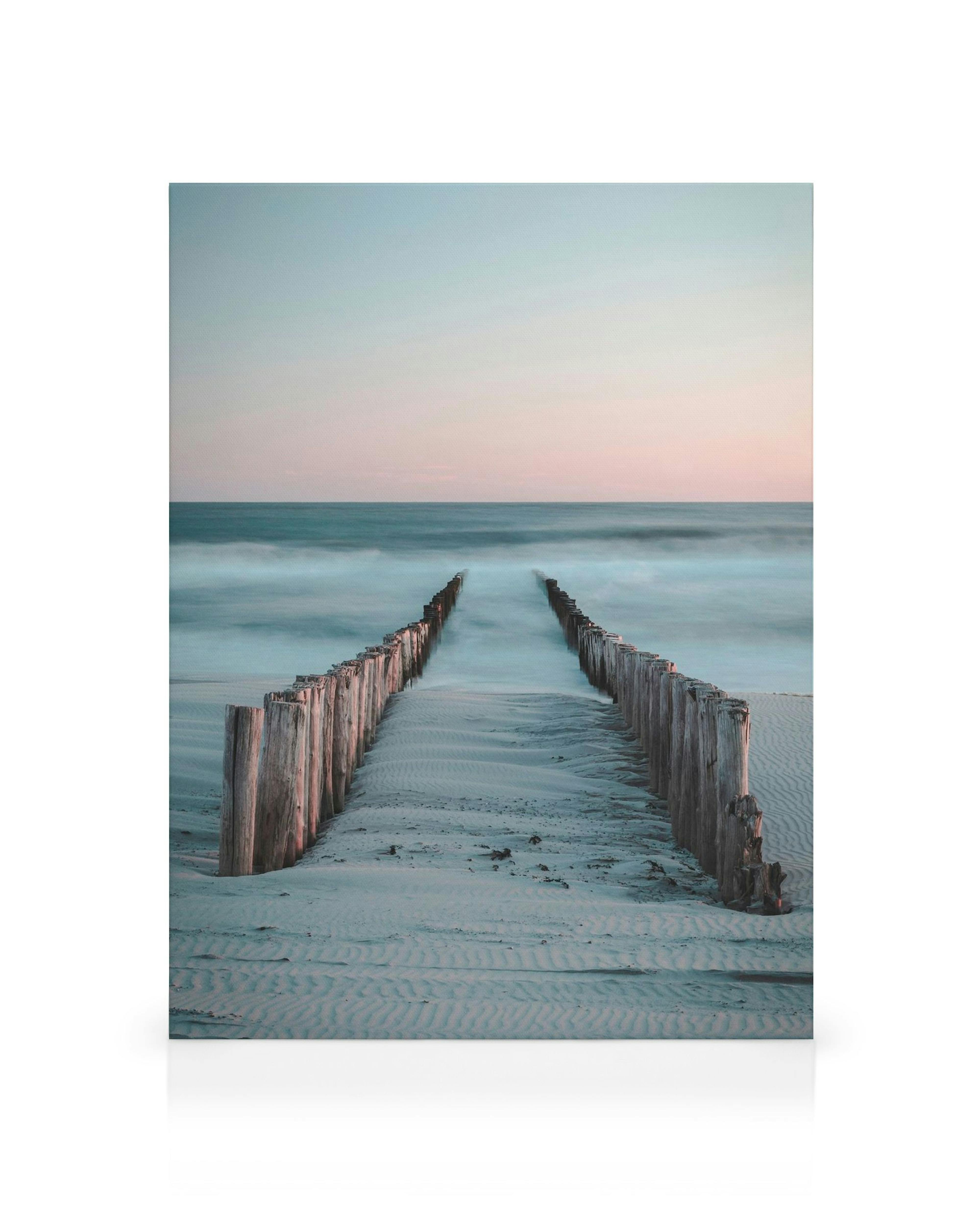 Κανβάς με ξύλινες πασσαλοσειρές στην άμμο, απαλά κύματα και ροζ-μπλε ουρανό