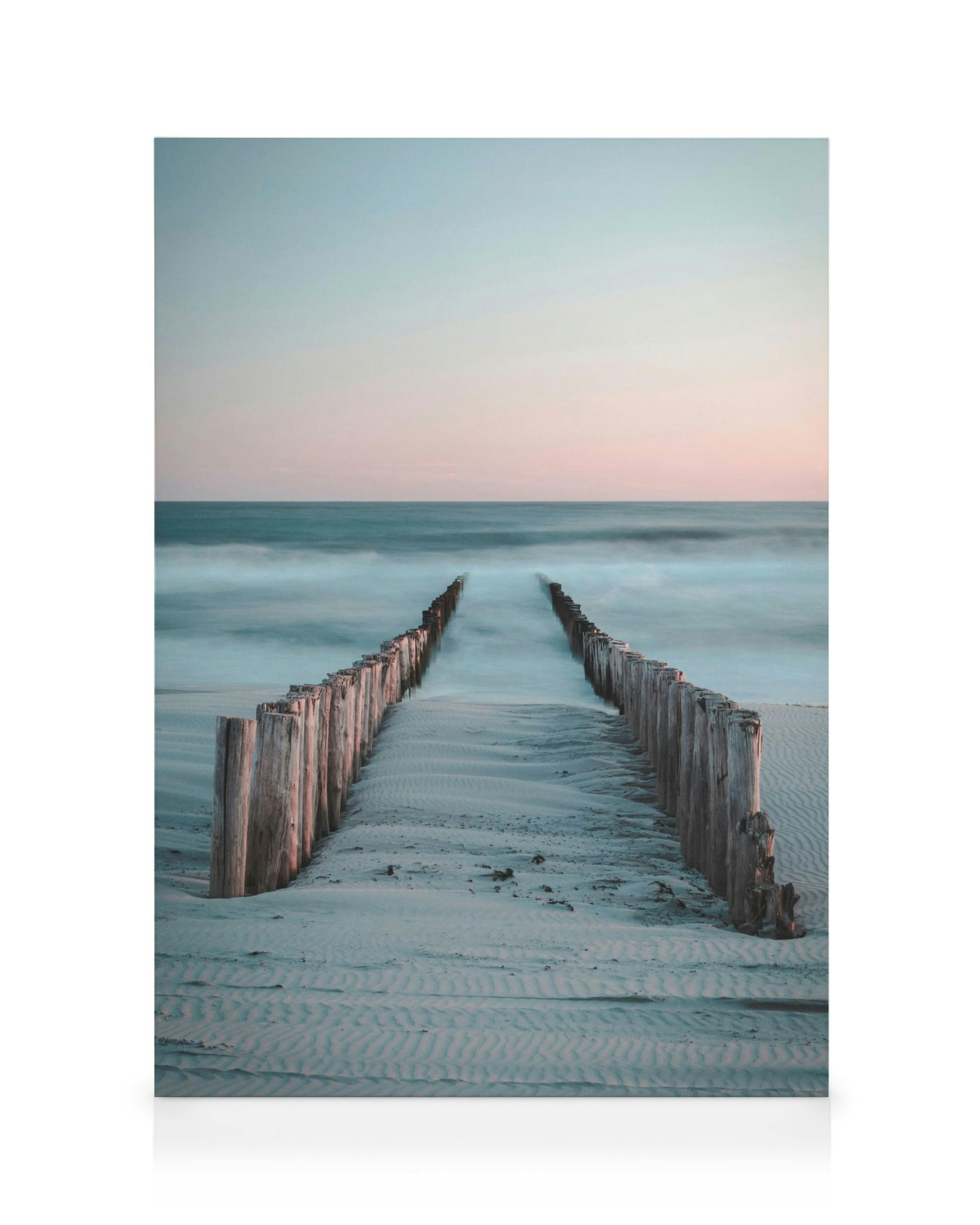 Toile dun quai en bois menant à la mer avec vagues floues bleues, ciel rose et beige, sable gris avec ondulations.