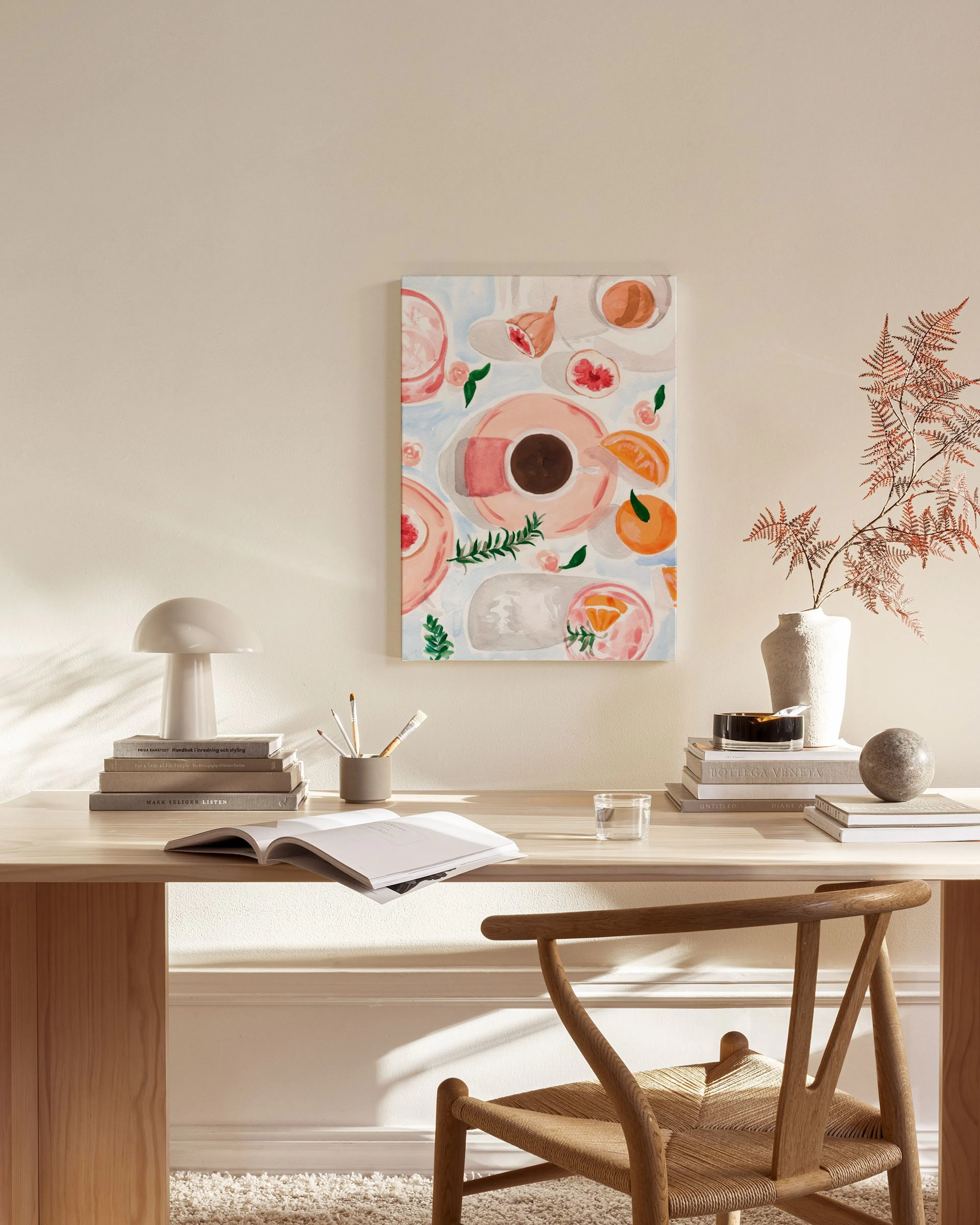 A colorful art print of a coffee cup, pink grapefruit, and oranges on a table, displayed in a minimal living room.