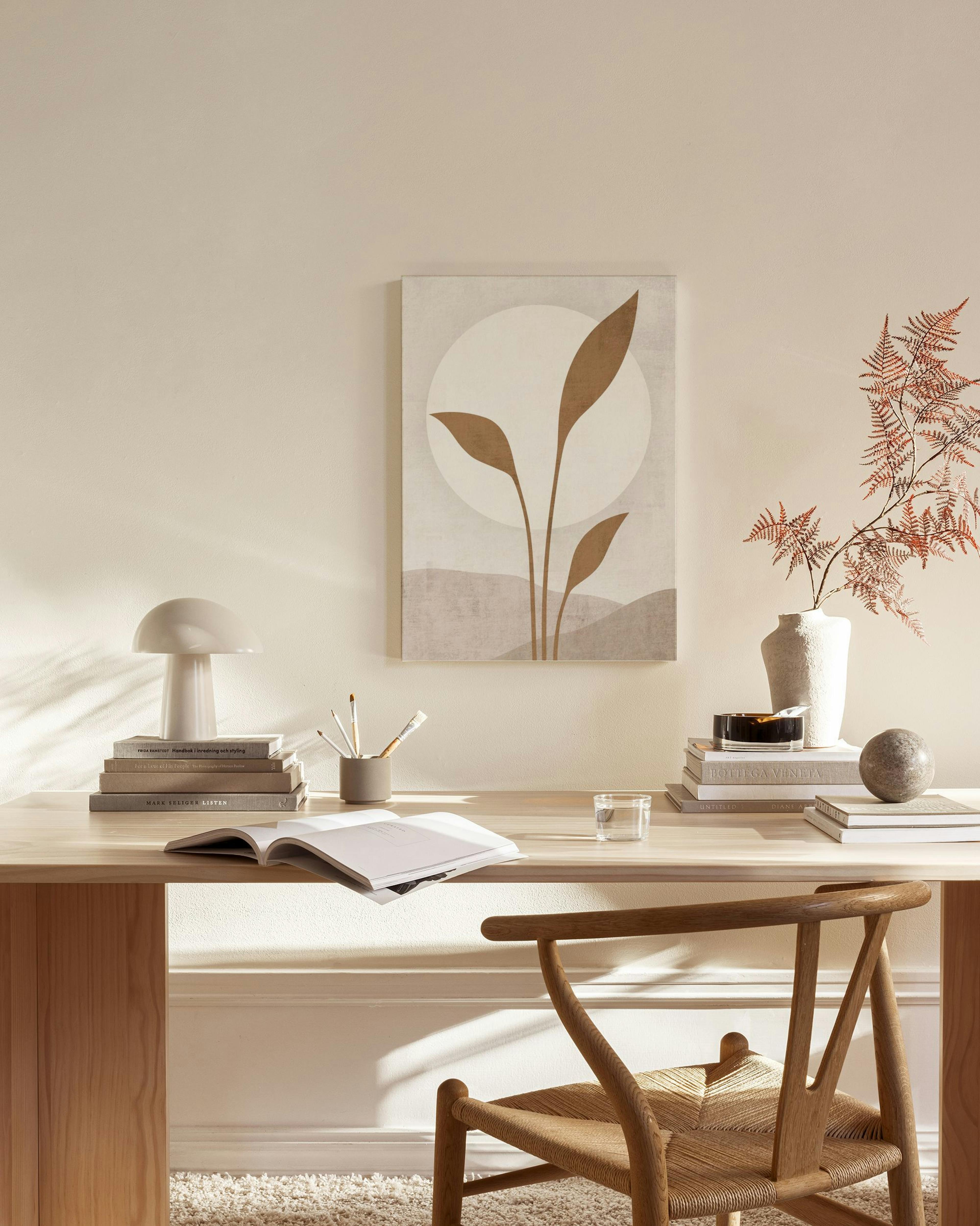Minimalist canvas print with brown plant shapes against a white circle and earthy background, hanging in a neutral living room.