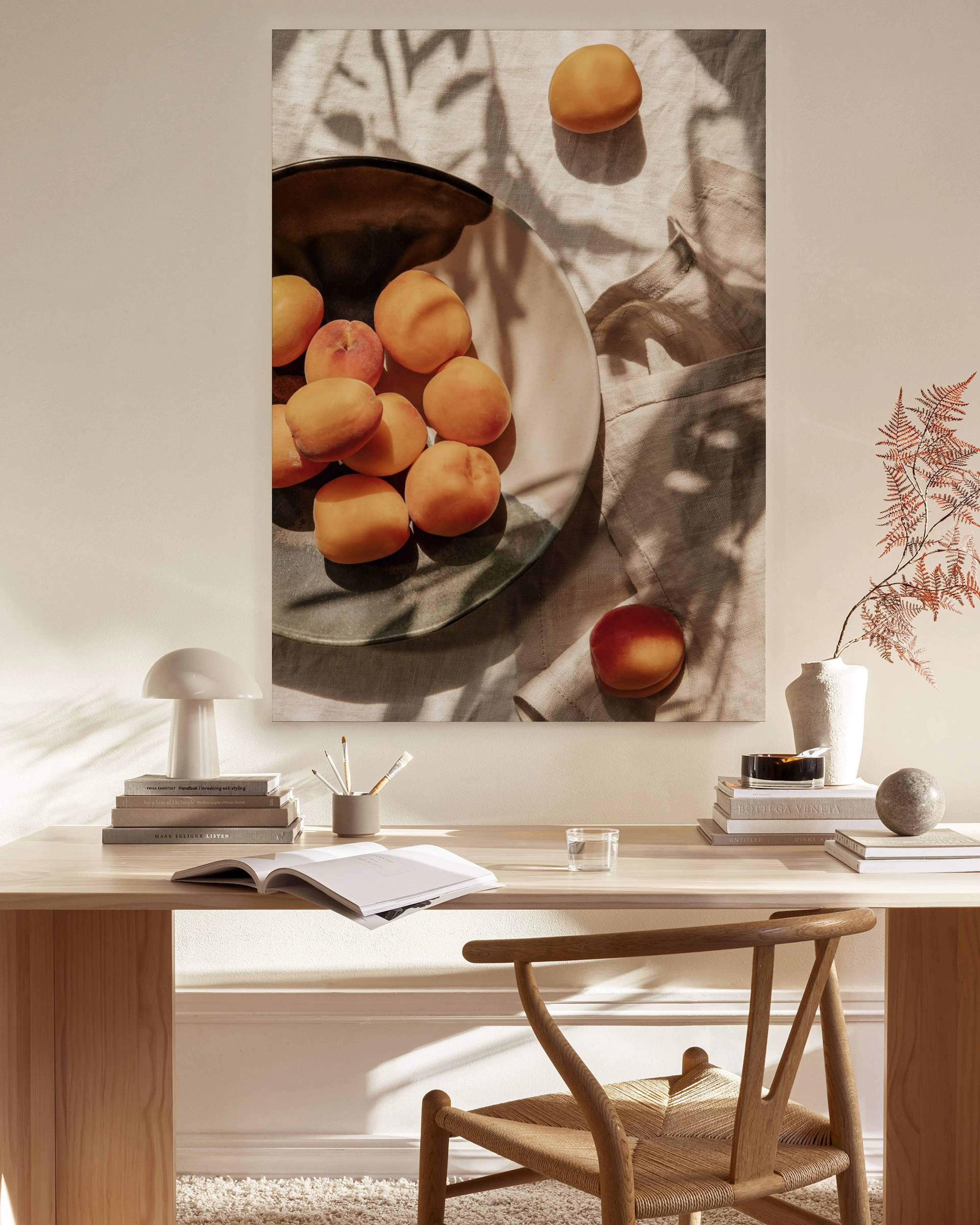 Toile murale de pêches et prunes dans un bol, avec des ombres de feuilles, affichée dans un salon moderne.