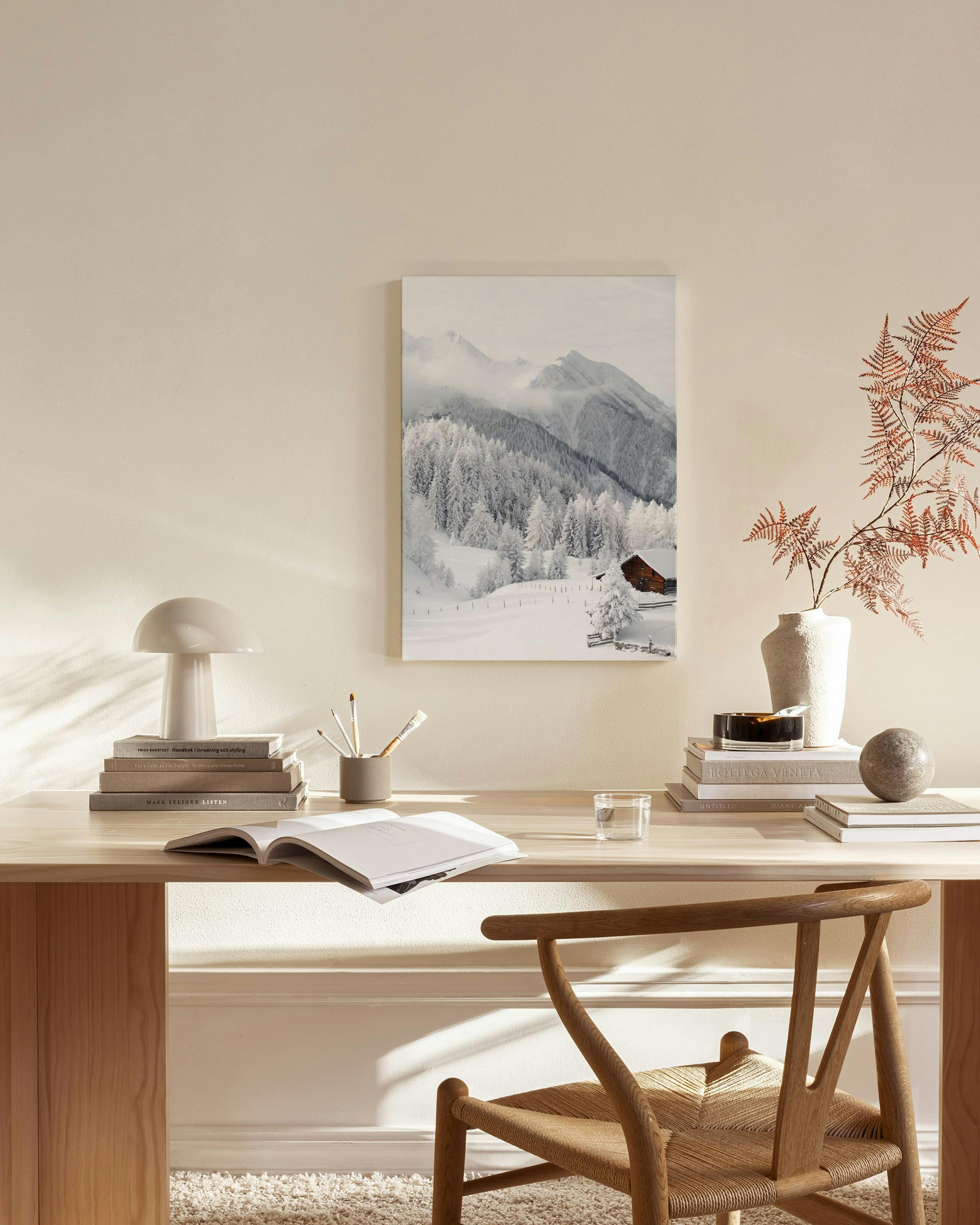 Obraz na plátne zobrazujúci zasnežené hory a lesy s chatou, zavesený v obývačke nad drevenou komodou.