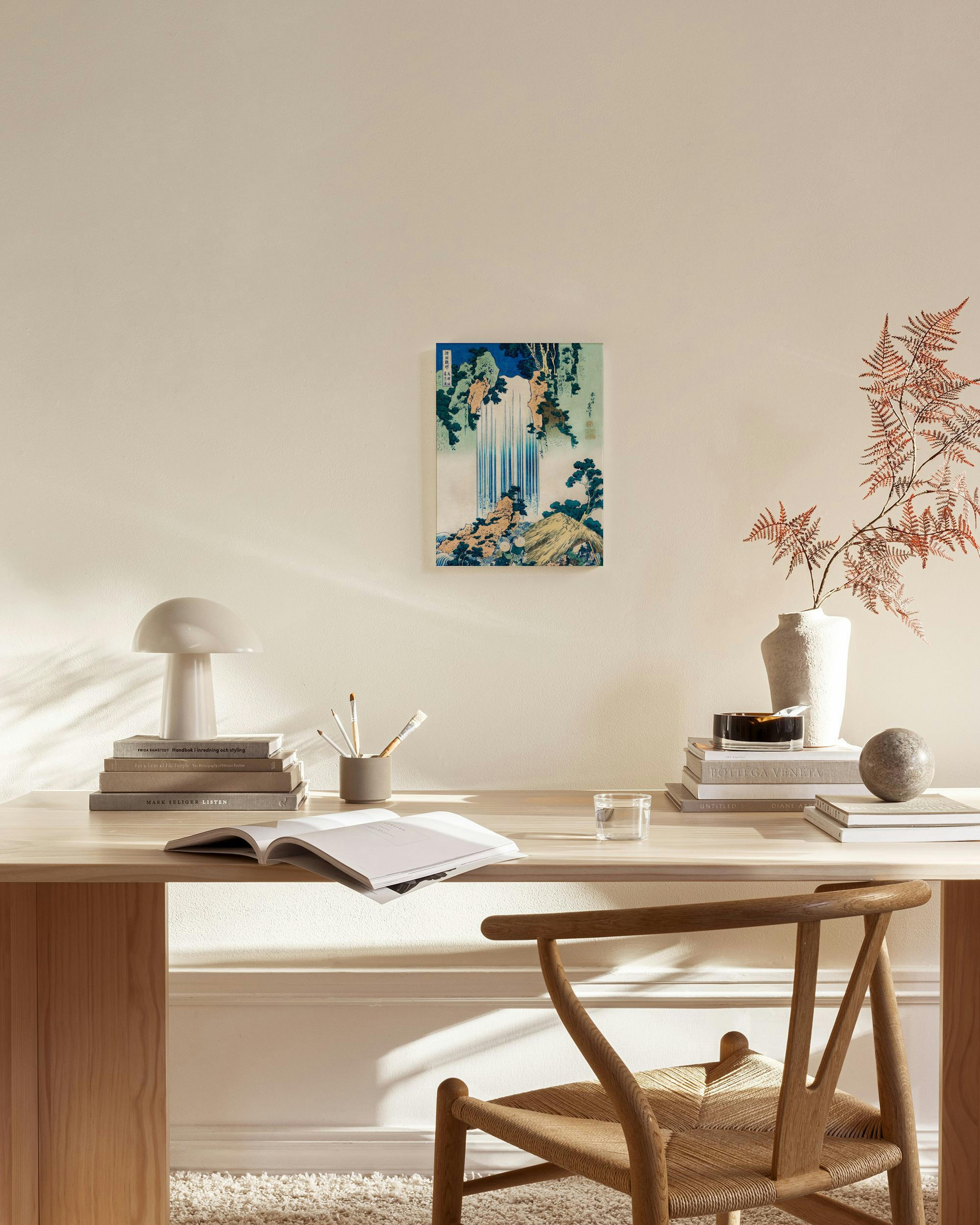 Japanese woodblock print of a waterfall cascading down a cliff with green foliage, hanging in a modern living room.