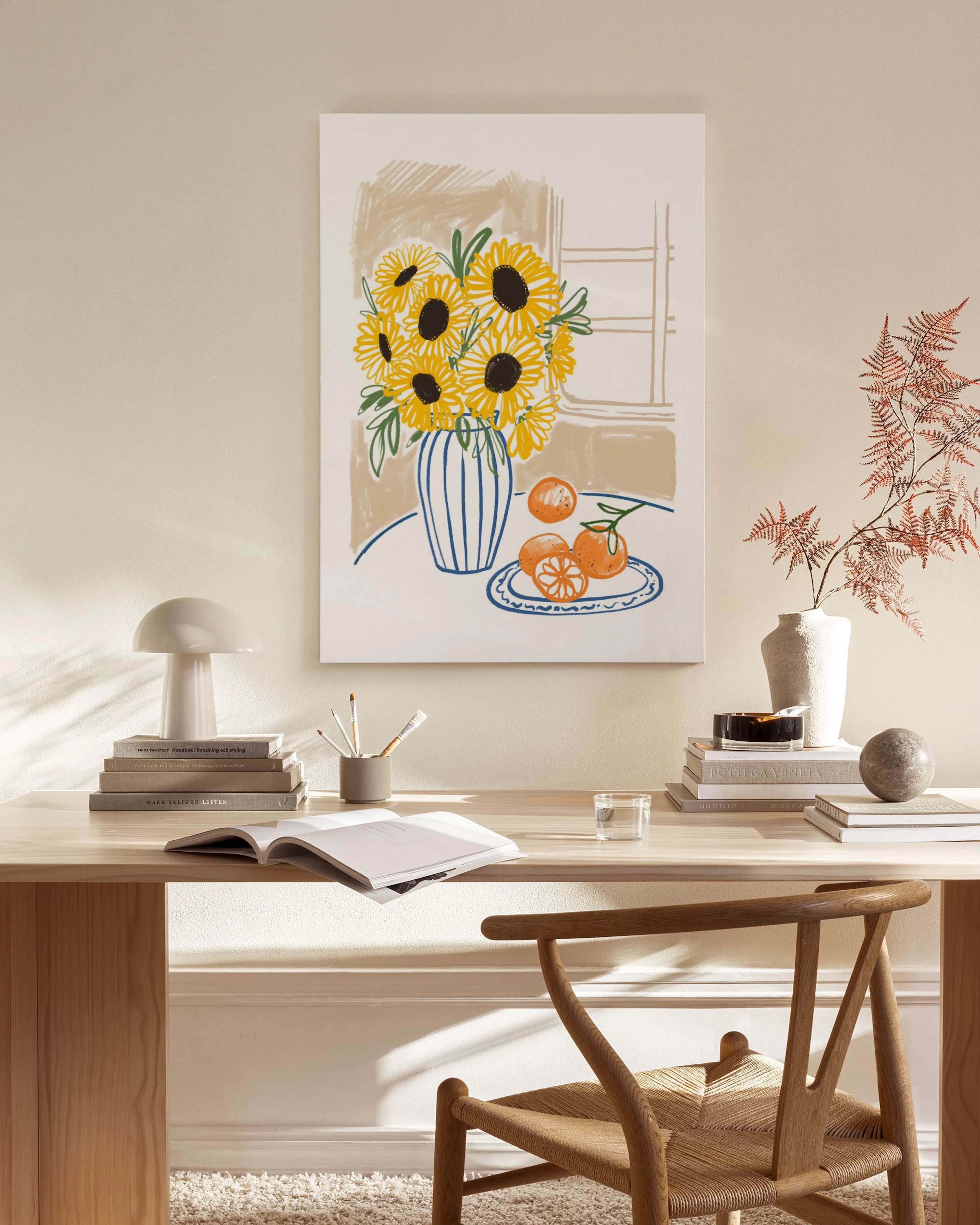 A canvas print of sunflowers in a striped vase with oranges on a plate, displayed in a bright living room.