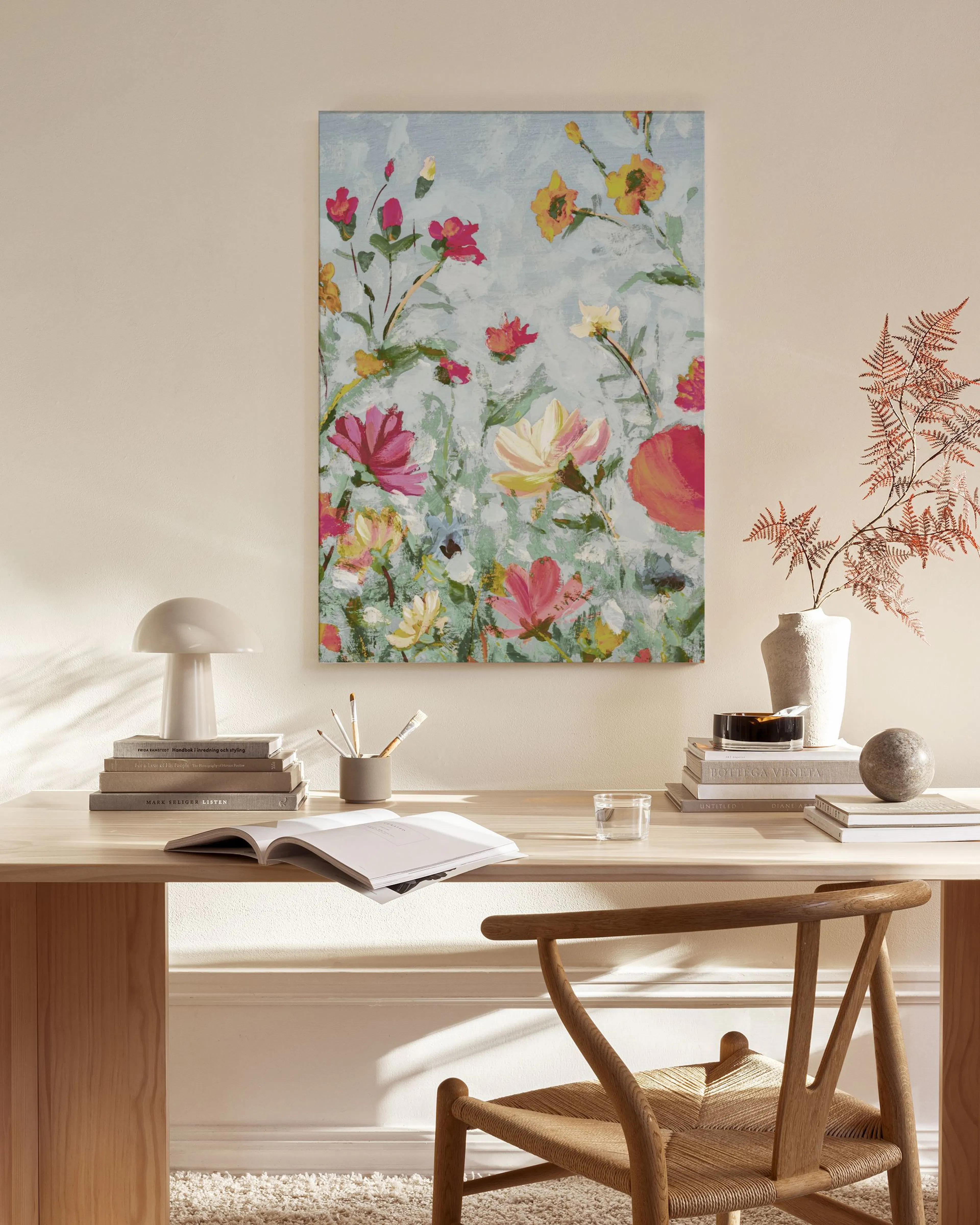 A vibrant floral canvas print with red, pink, yellow, and white flowers on a light blue background, hanging in a modern living r