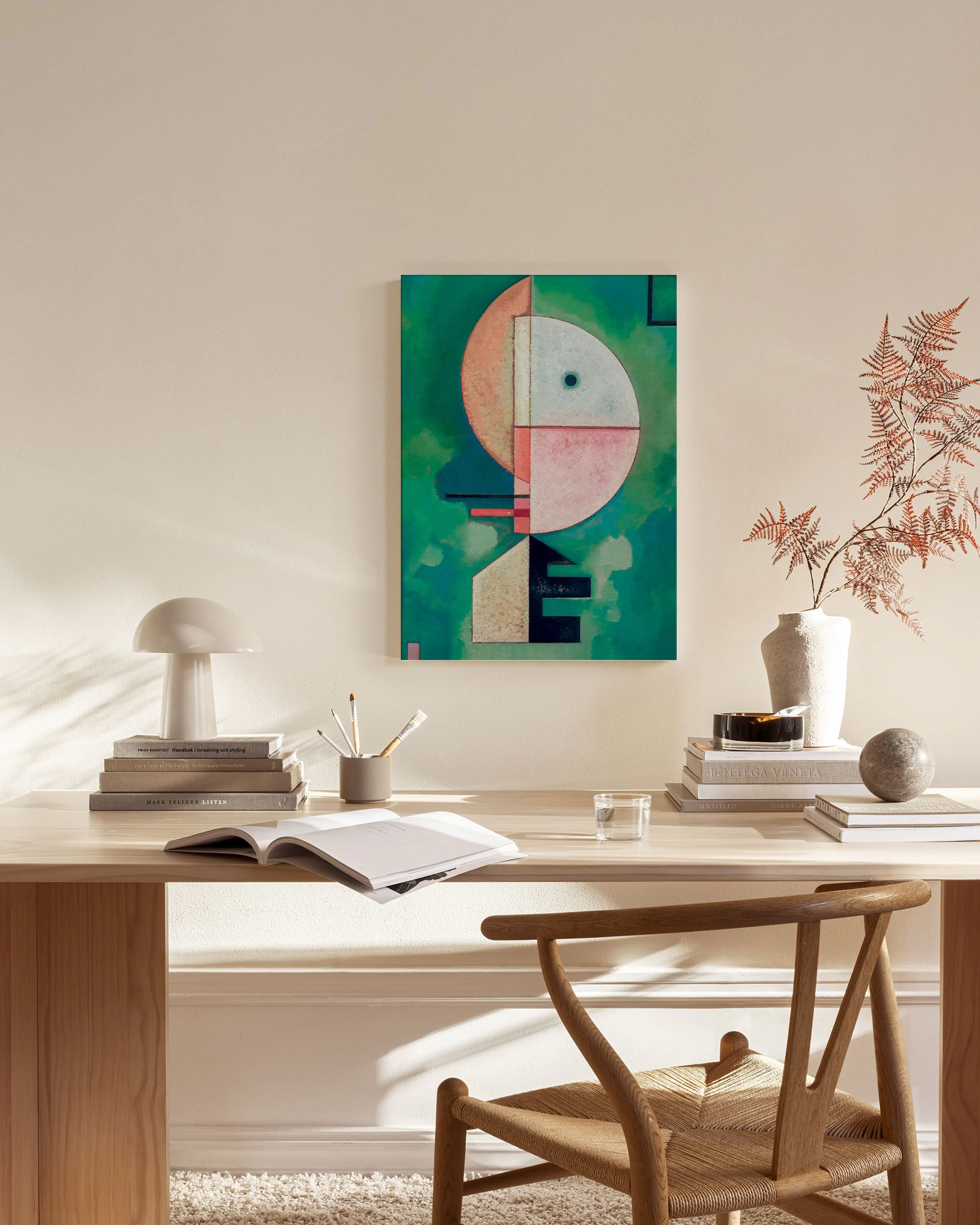 A canvas print with a green background features abstract shapes in pink, peach, and black, hanging in a minimalist living room.