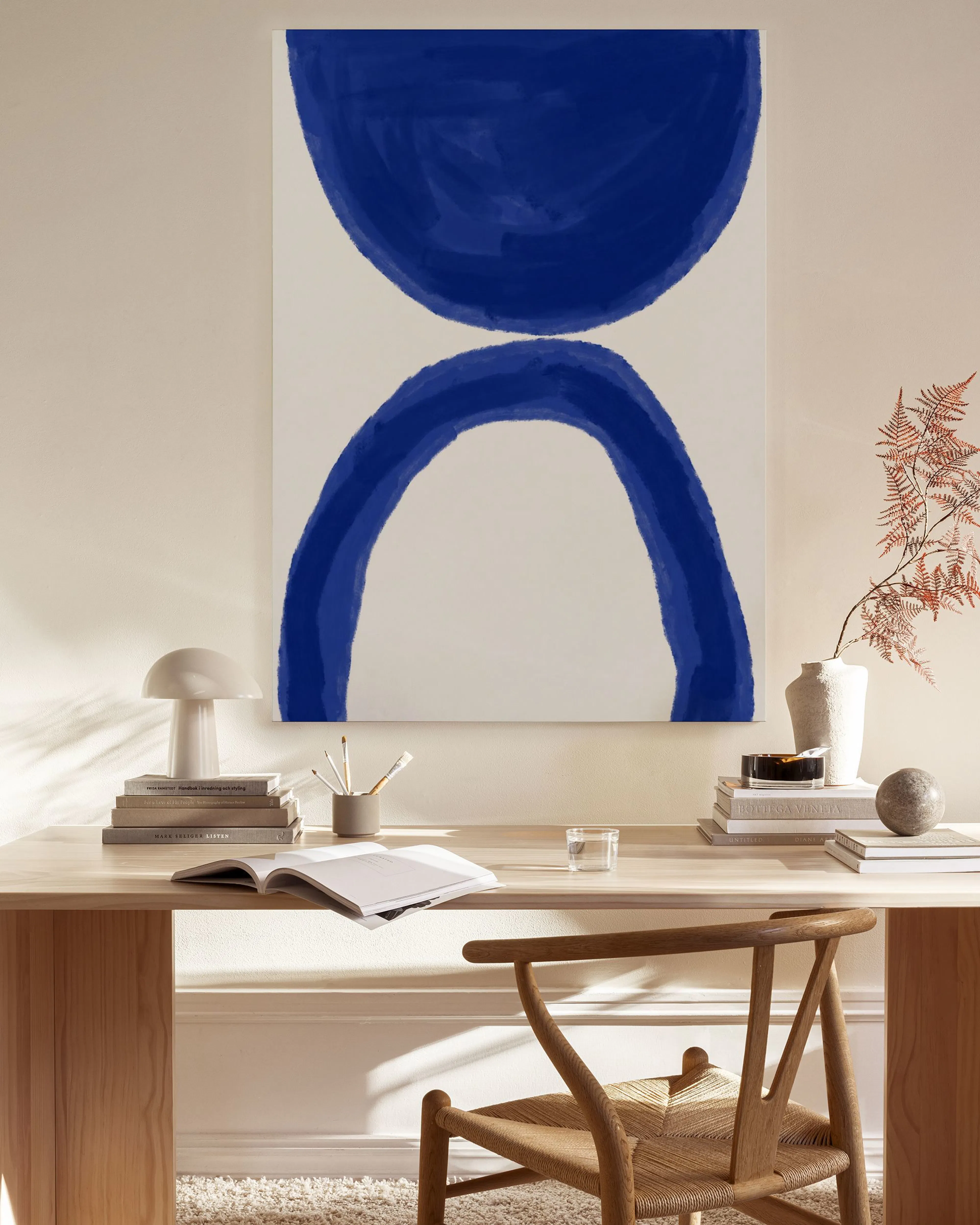 Blue abstract canvas print with a semi-circle and arch, hanging in a bright, minimalist living room.