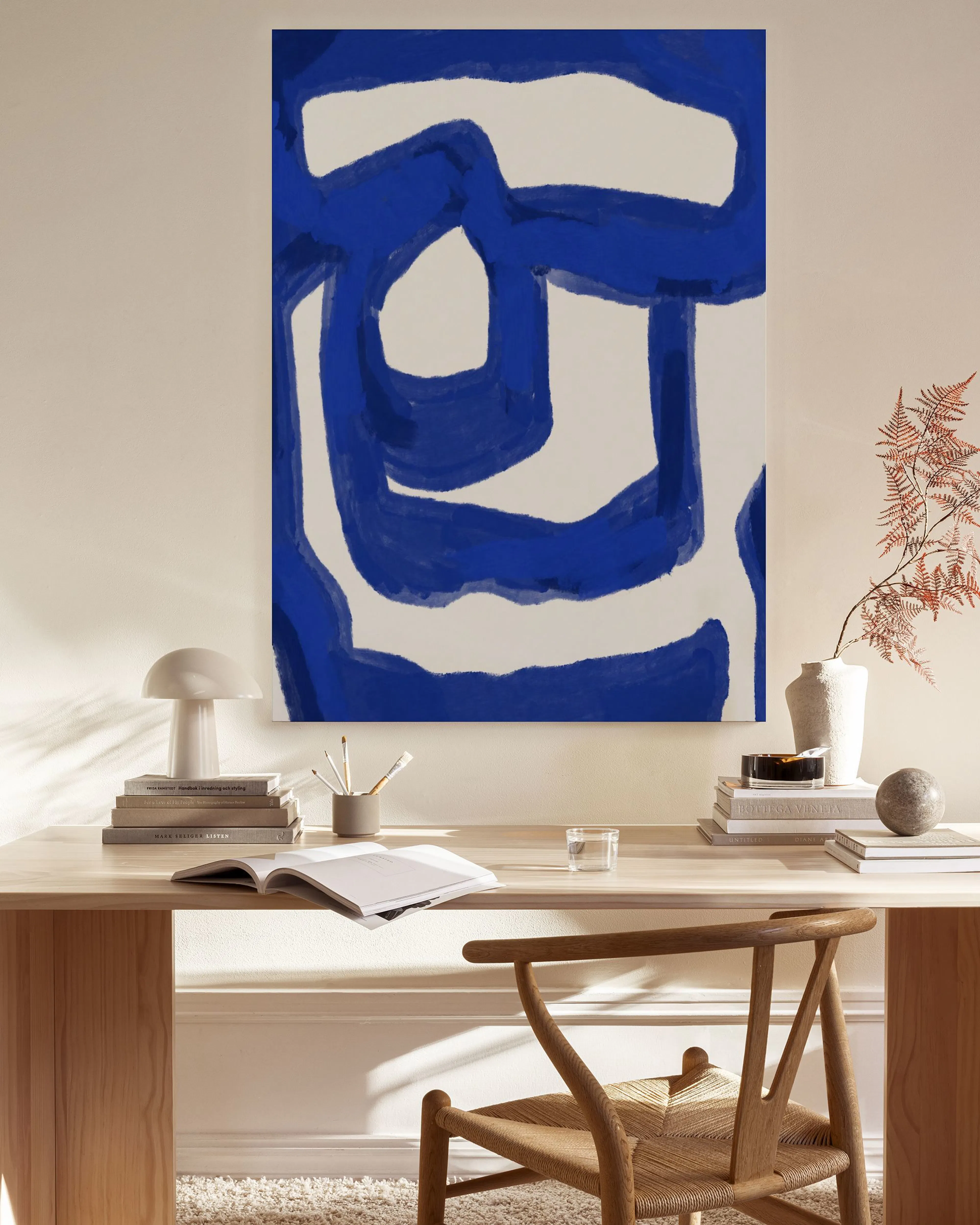 Abstract canvas print with bold blue organic shapes on a white background, hanging in a minimalist living room.
