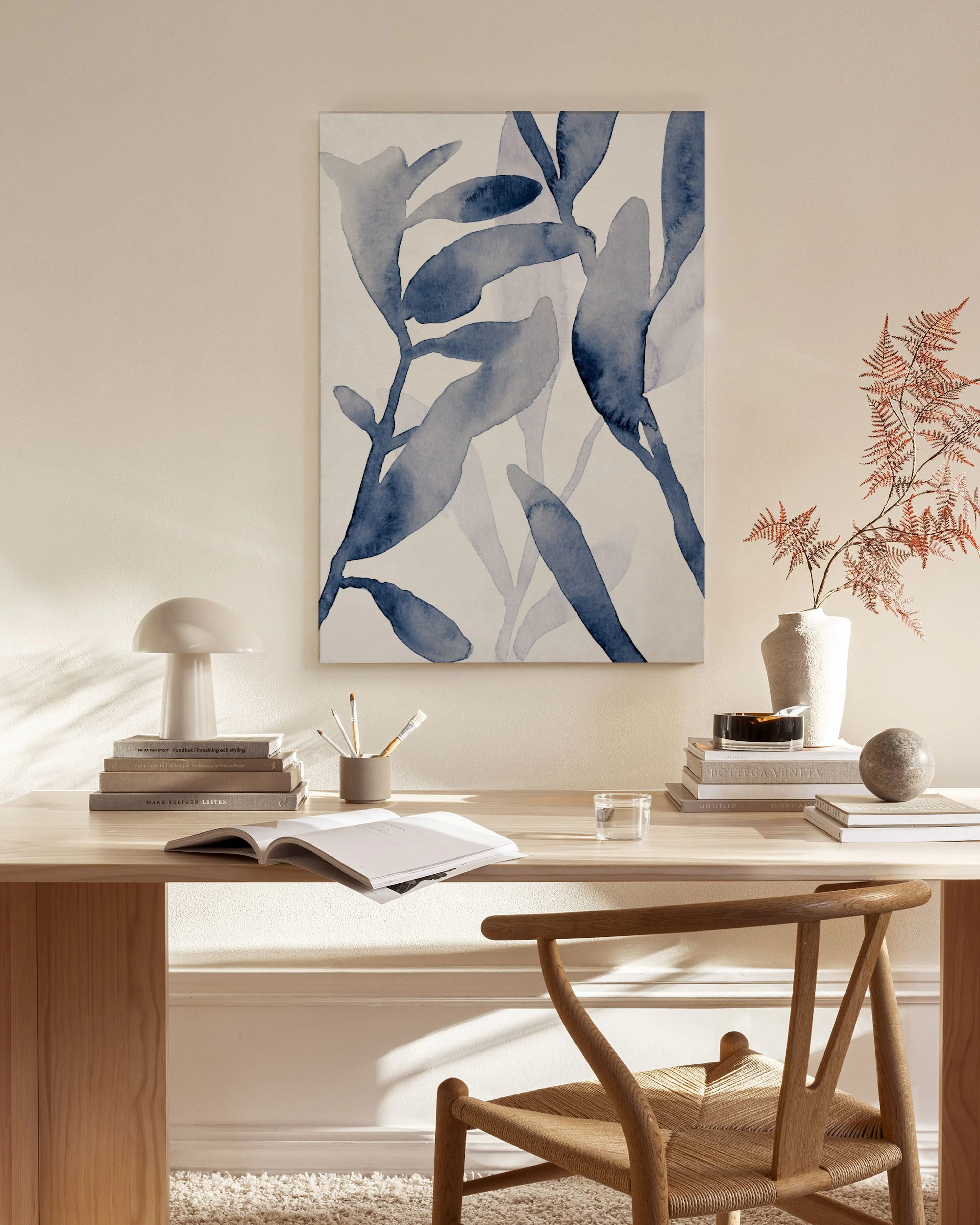 Lienzo floral azul de hojas de acuarela, colgado sobre un mueble bajo con una lámpara en una sala de estar minimalista.