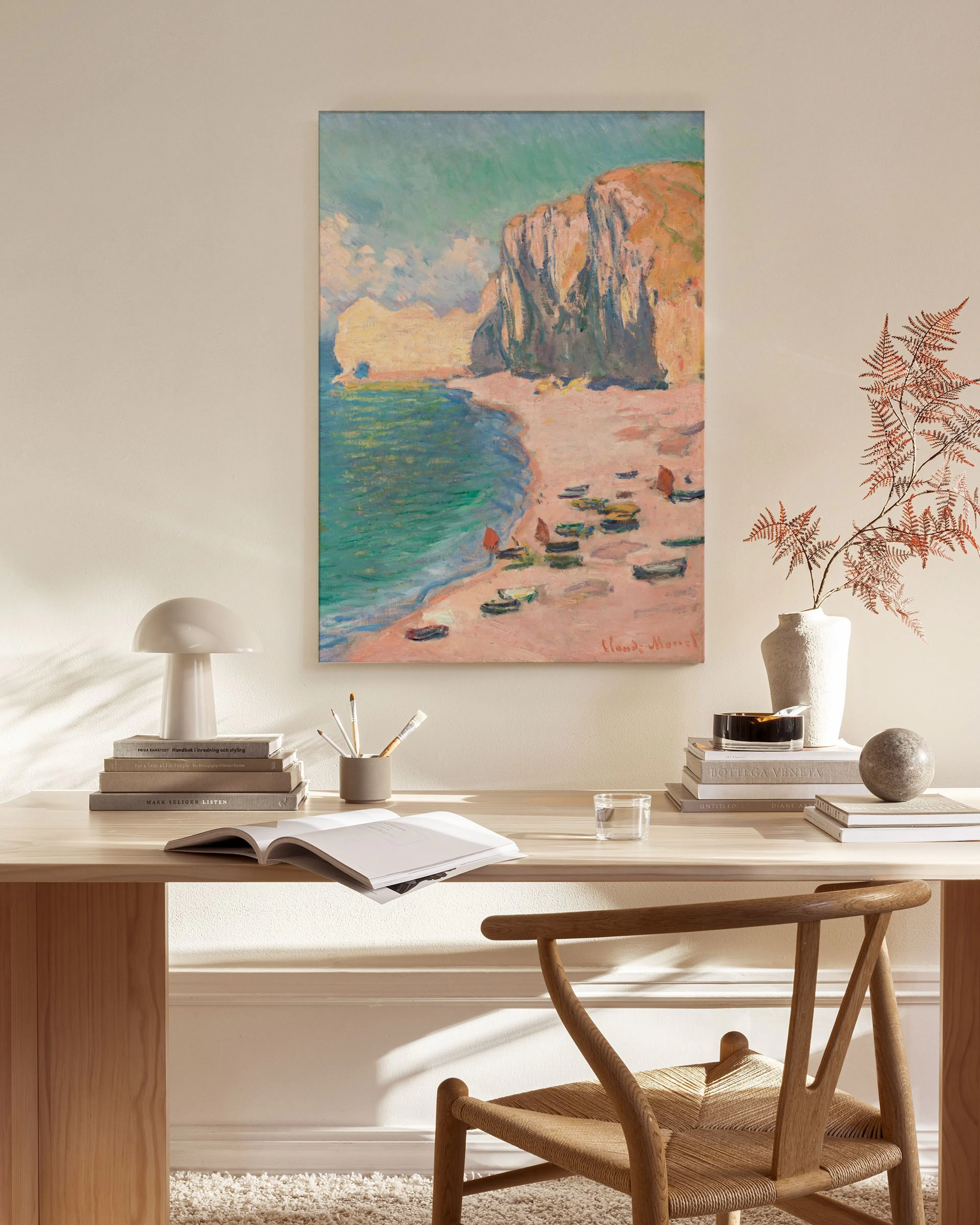 Lienzo de playa con acantilados y barcas en tonos azules y tierra, colgando sobre un mueble bajo en un salón escandinavo.
