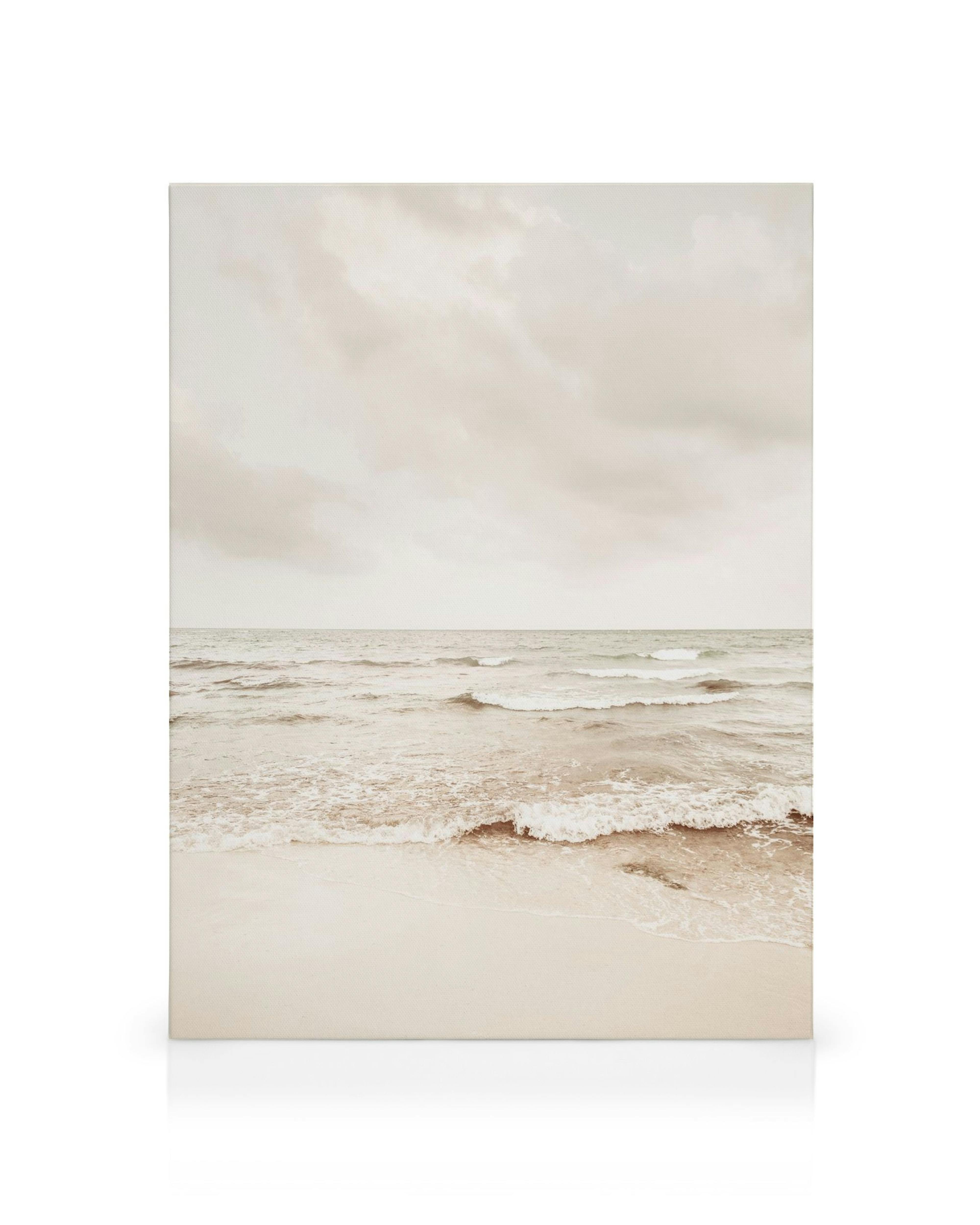 Canvas print of a tranquil beach scene with gentle waves on smooth sand under an overcast sky, in muted beige and blue.