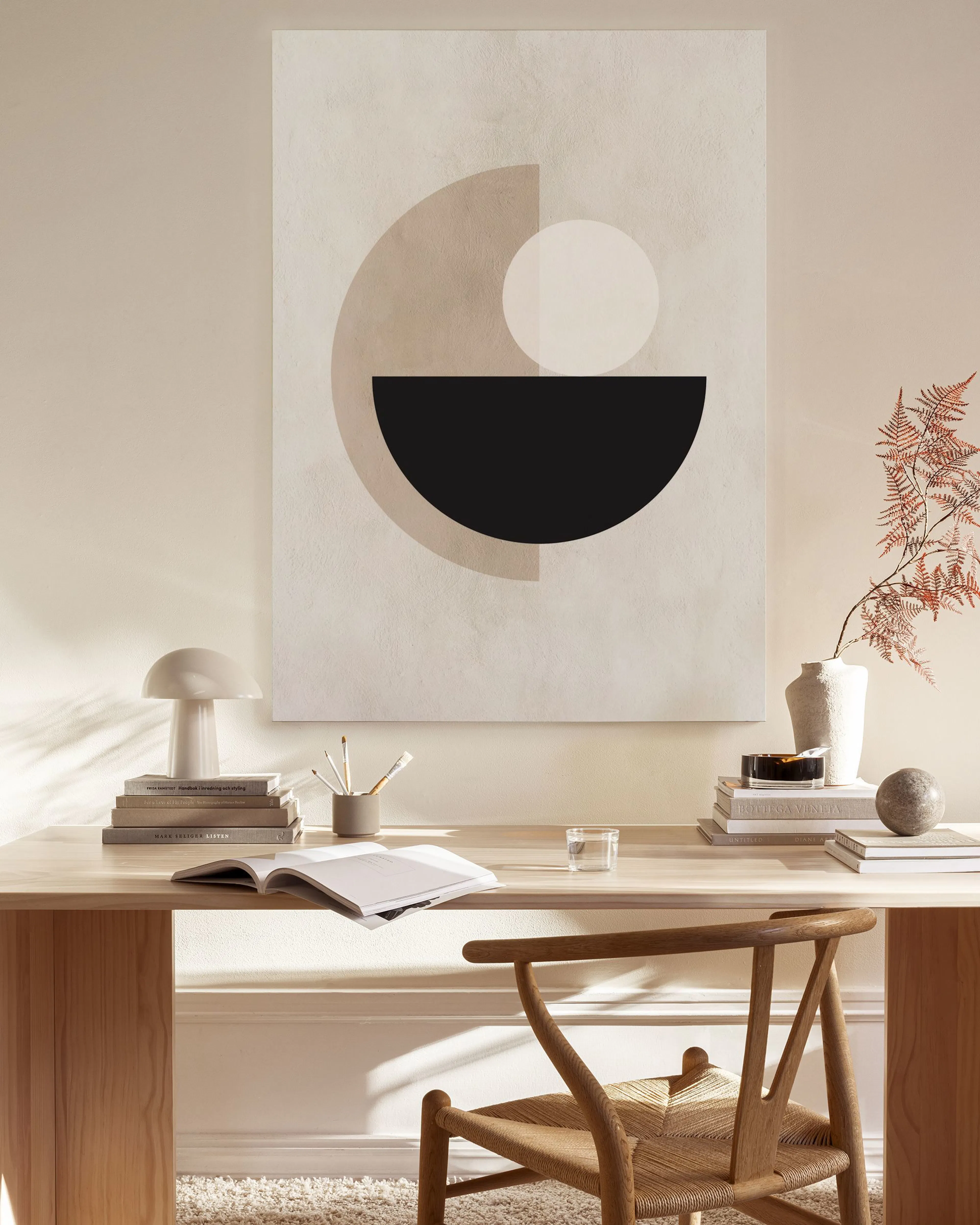Canvastavla med geometriska former i svart, vitt och beige, hängandes i ett ljust vardagsrum ovanför en bänk.