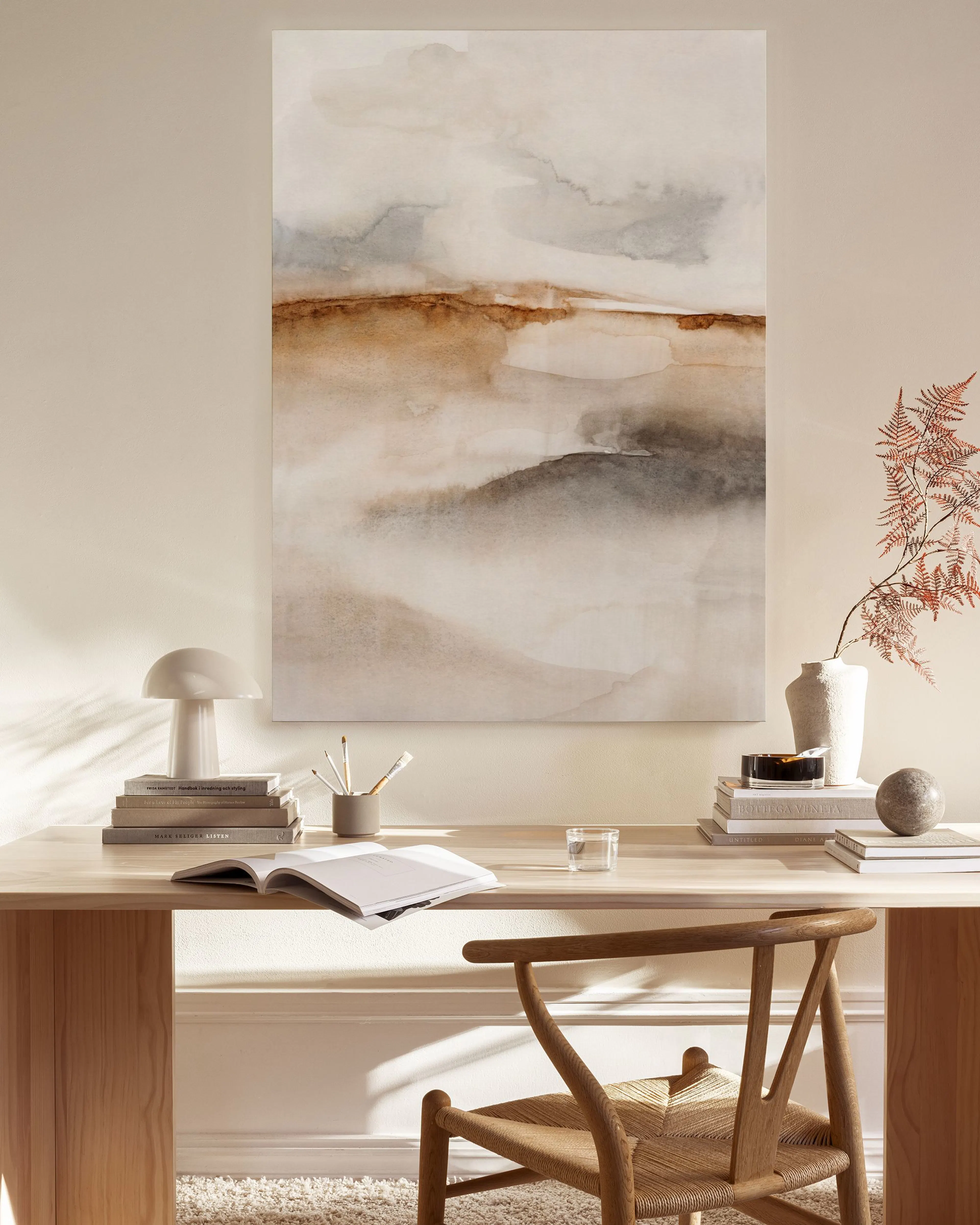 A canvas print with abstract brown, grey, and beige landscape forms, displayed above a wooden console table in a neutral-toned l