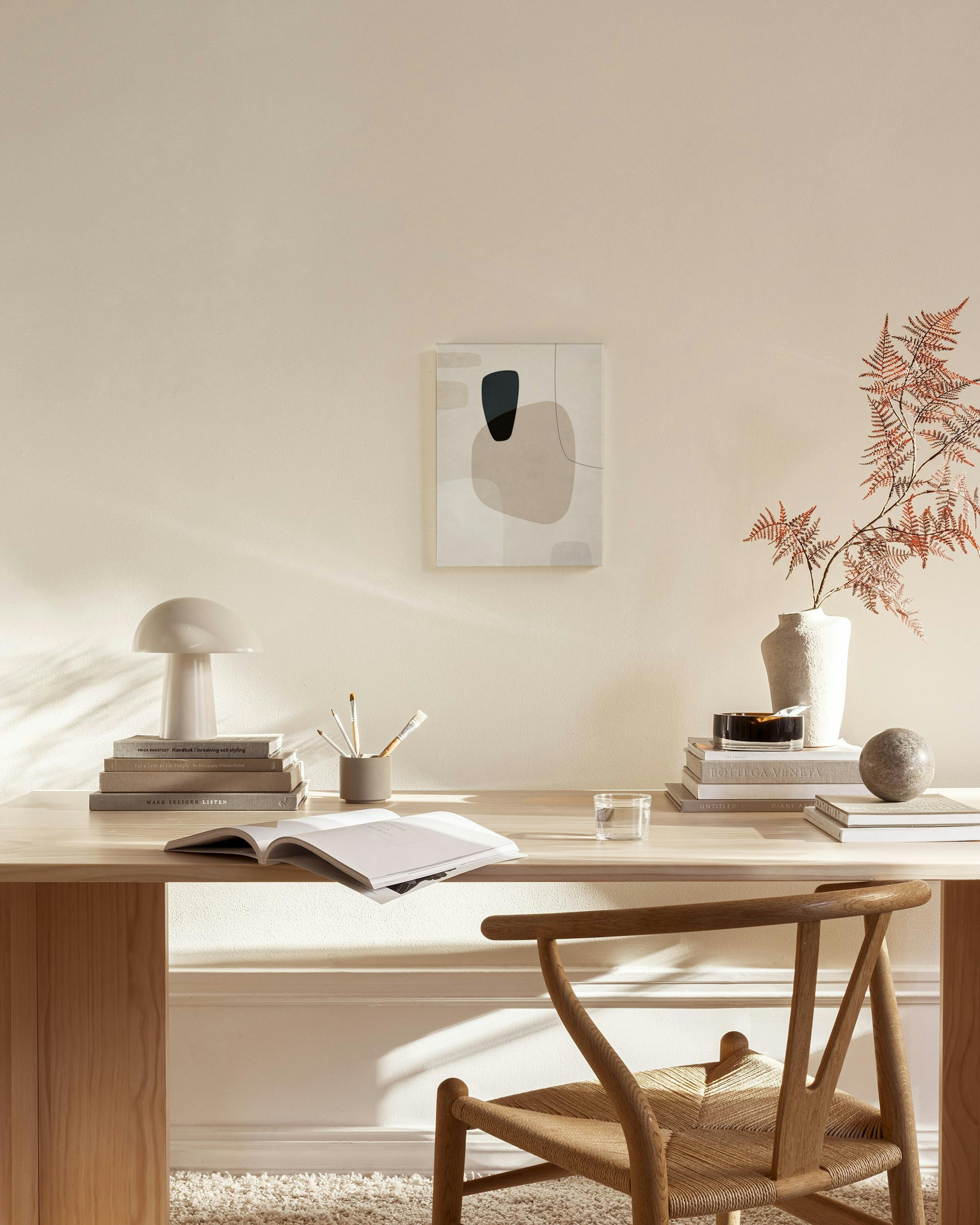 Lienzo con formas orgánicas en tonos neutros y líneas negras, colgado sobre un mueble bajo en una sala.