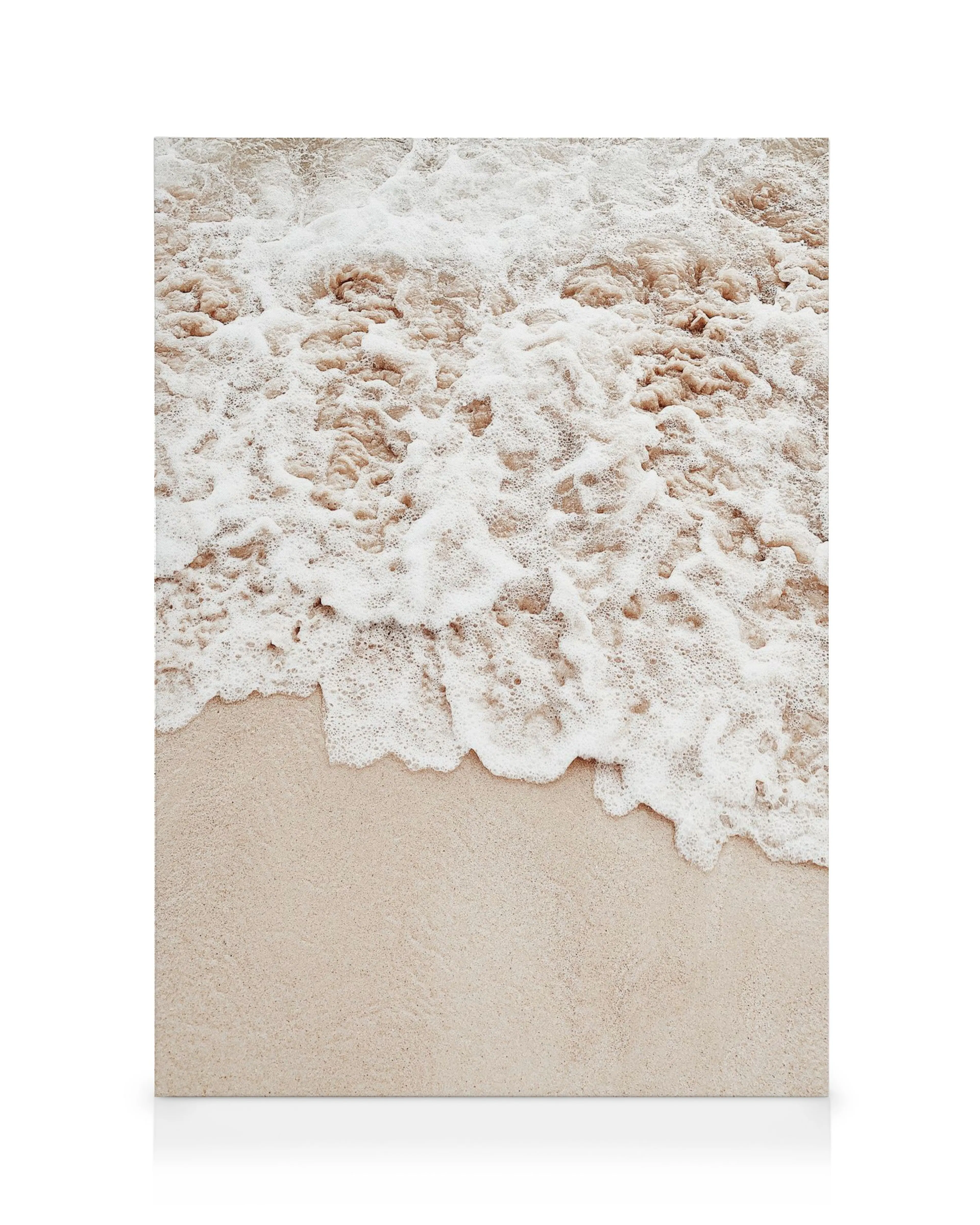 Vågor som kraschar mot en sandstrand, med vitt skum över mörkbrunt vatten som möter ljusbeige sand. Hav, strand, vågor.
