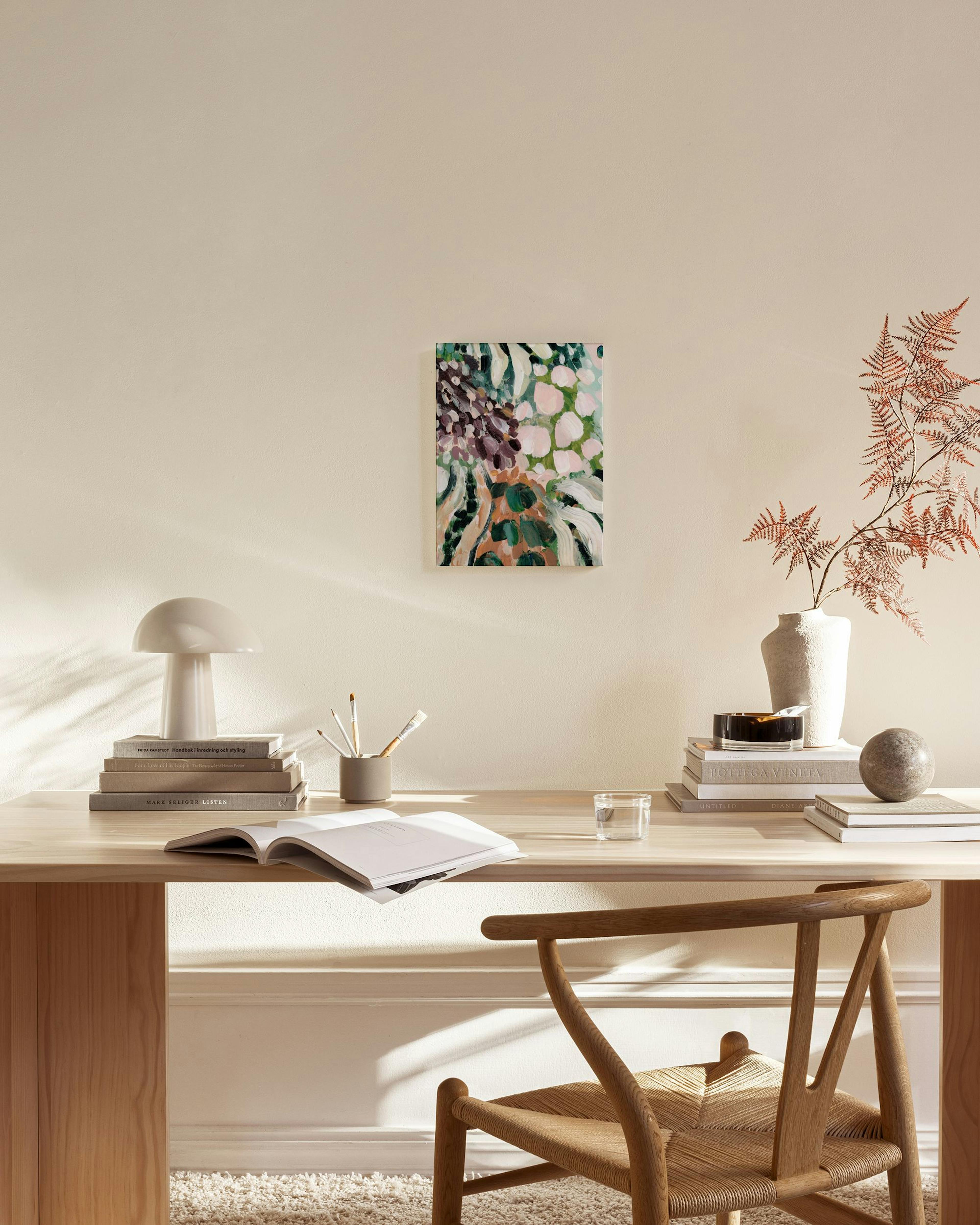 An abstract canvas print with organic shapes in pink, green, and dark purple, displayed in a bright modern living room.