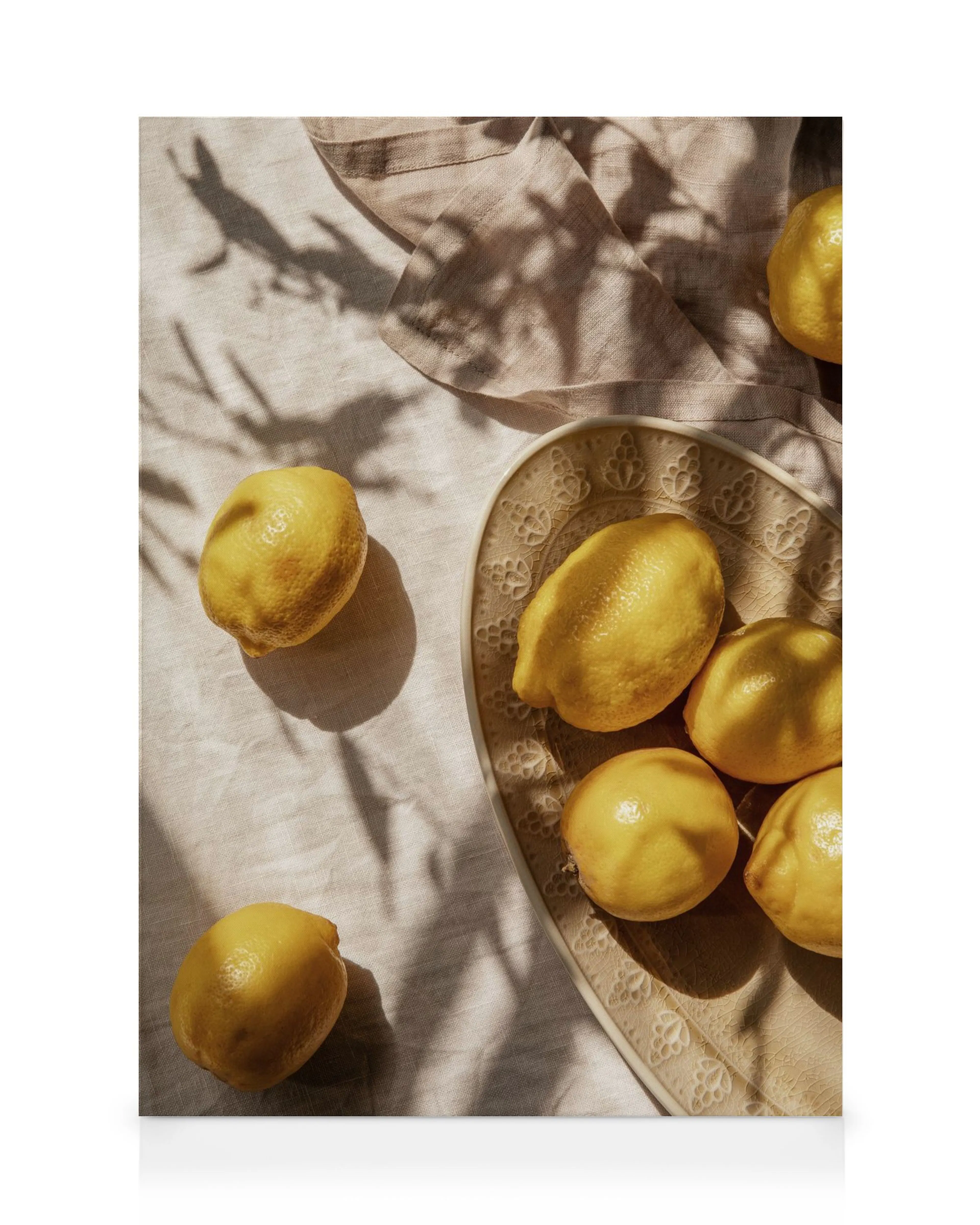 Limoni gialli su piatto in pizzo e tessuto beige, illuminati dal sole, con ombre di foglie.