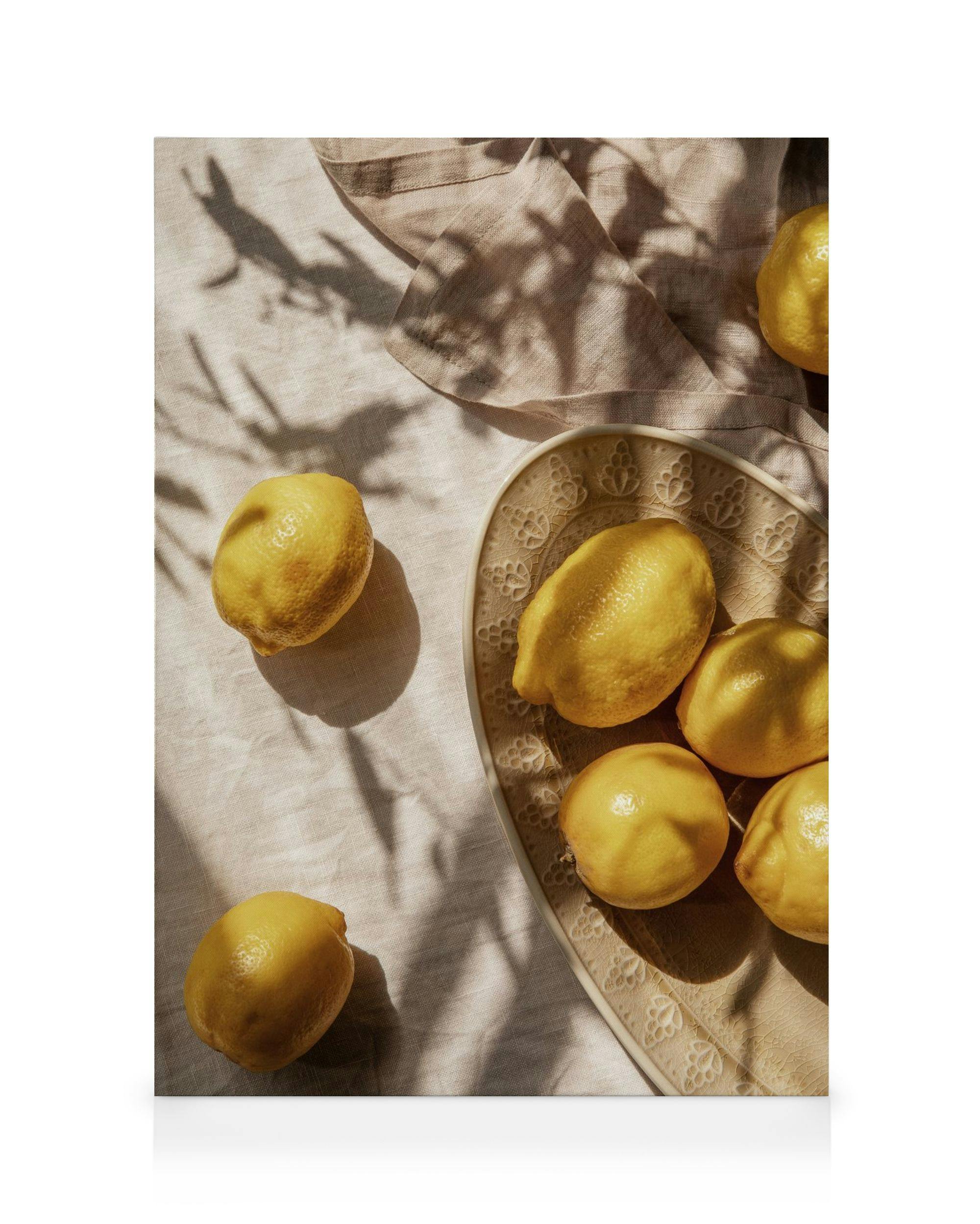 Vibrant yellow lemons on a heart-shaped plate and tablecloth, with sunlight shadows, on a canvas print.