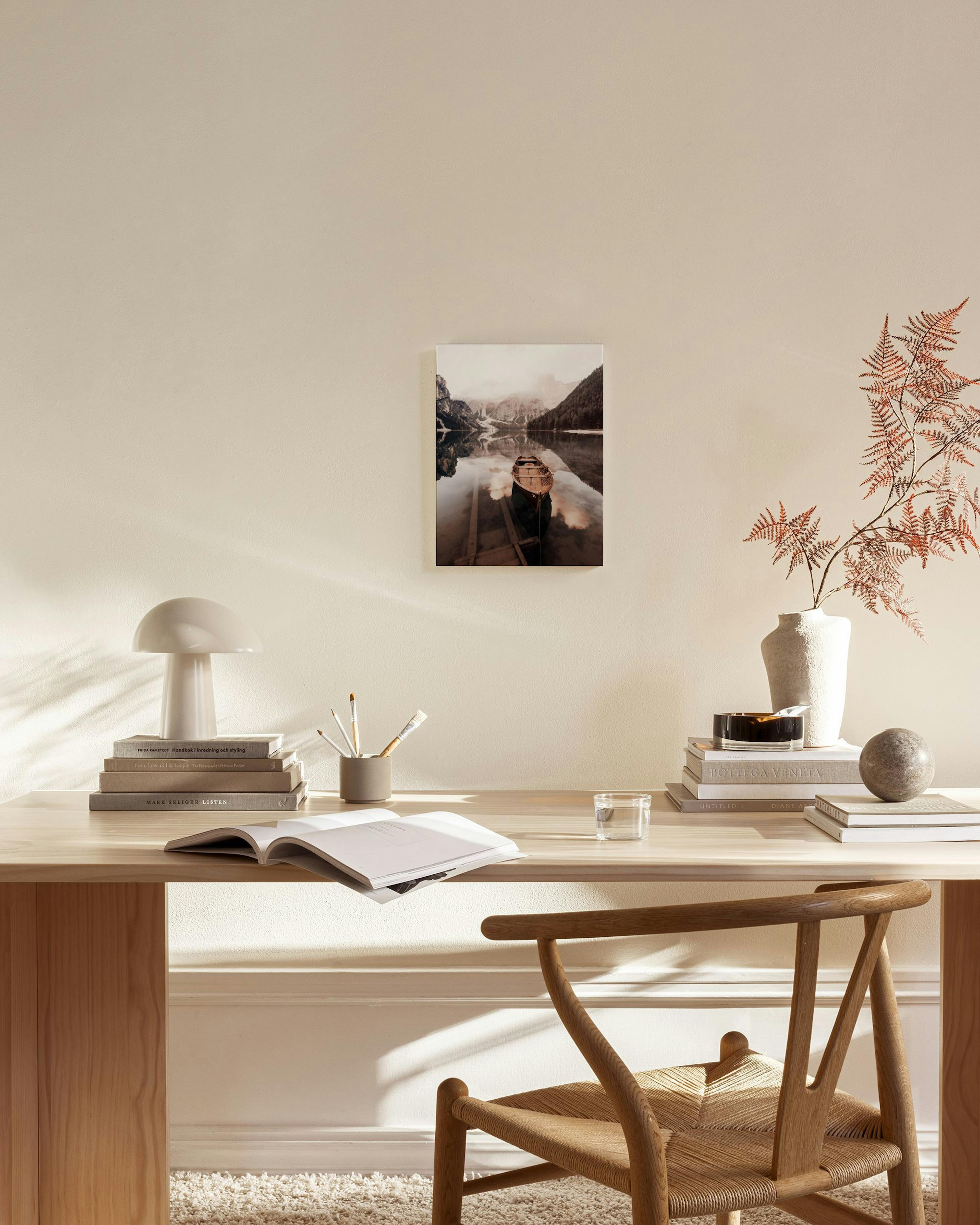 Een canvas van een houten roeiboot op een spiegelglad bergmeer, hangend in een neutrale woonkamer.
