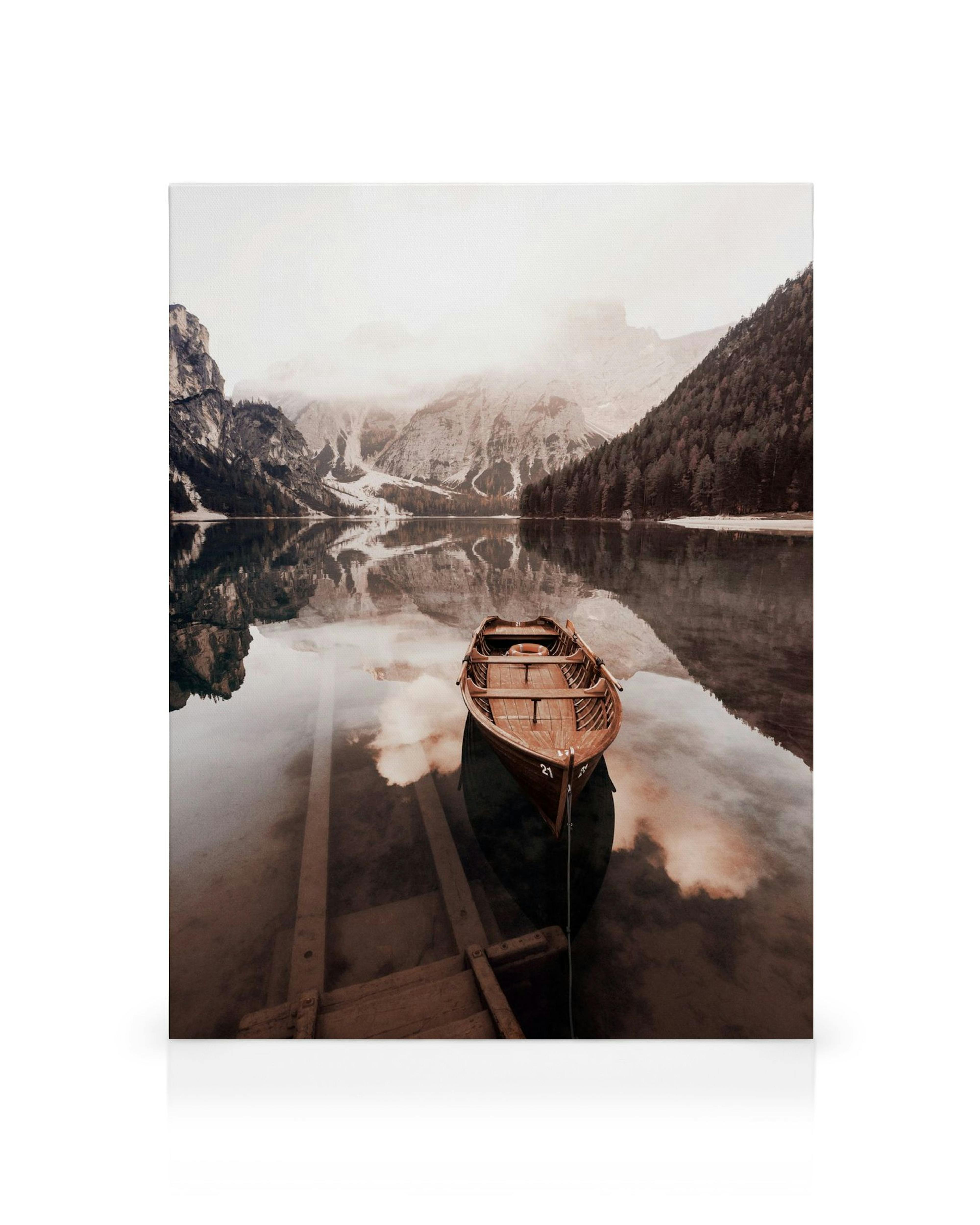 Canvas met houten boot op kalm meer, weerspiegelende bergen en wolken in gedempte bruin- en beigetinten.