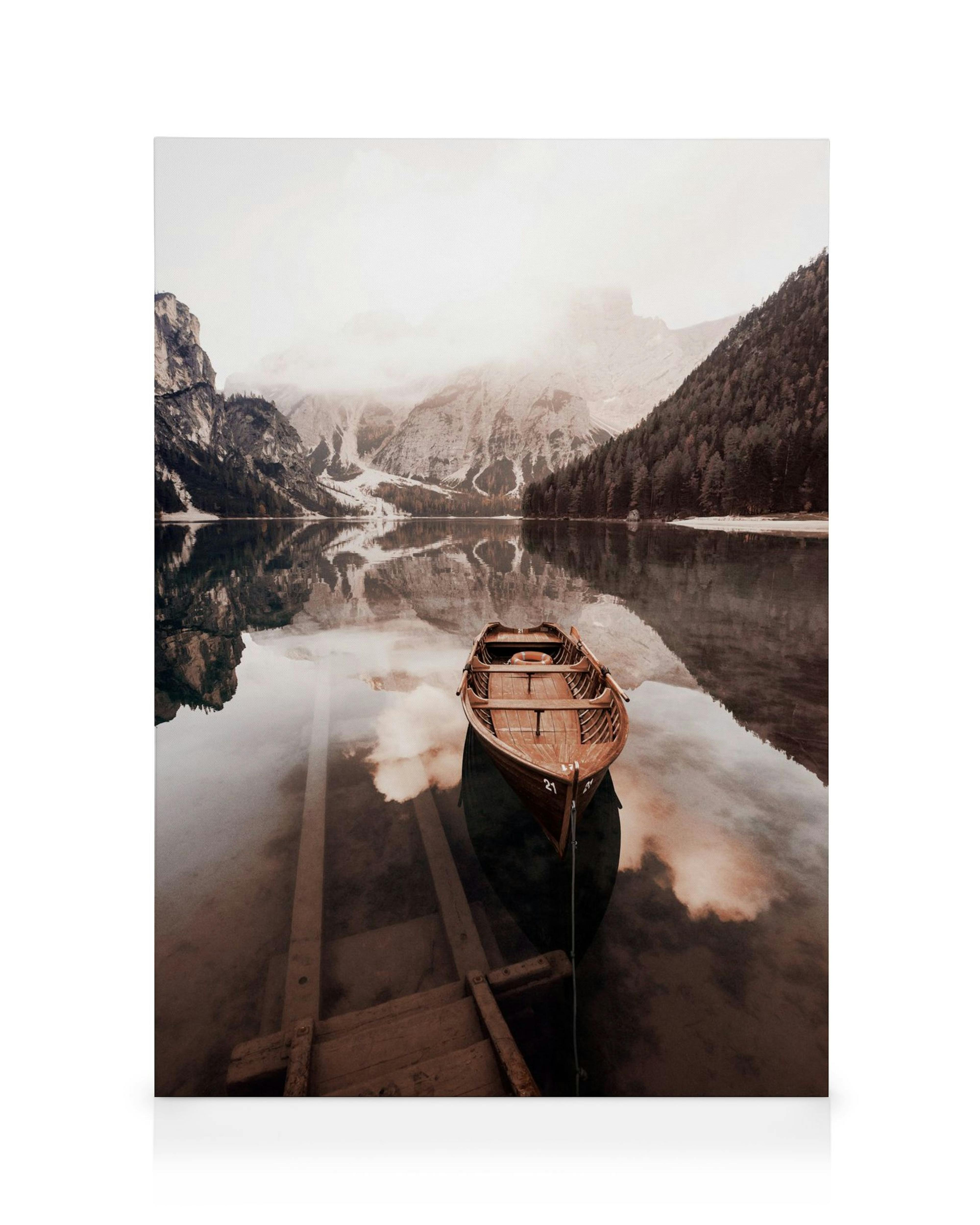 Wooden boat on a still lake, reflecting misty mountains and clouds in muted, serene tones.
