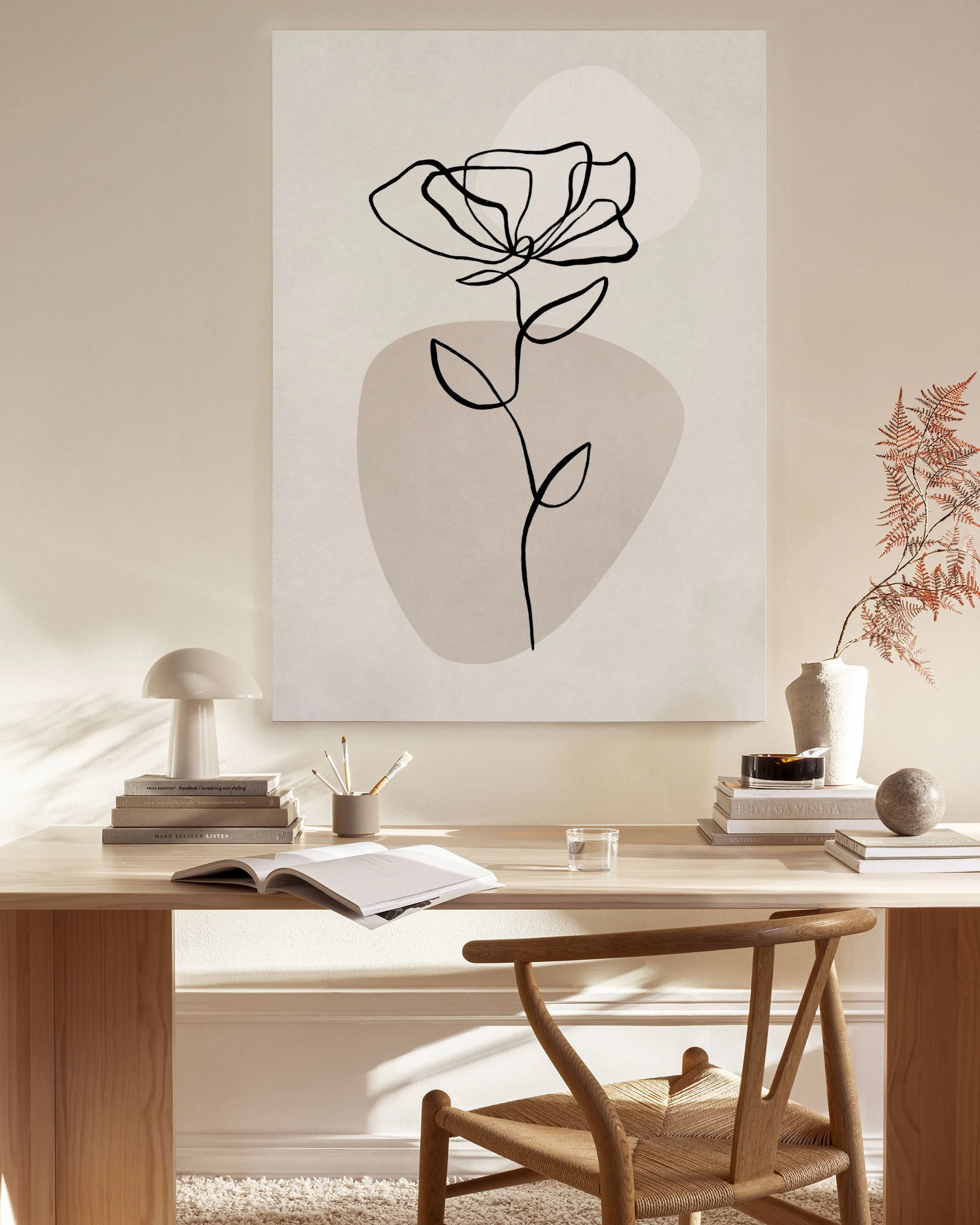 Toile florale minimaliste noire sur fond beige clair, dans un salon moderne.