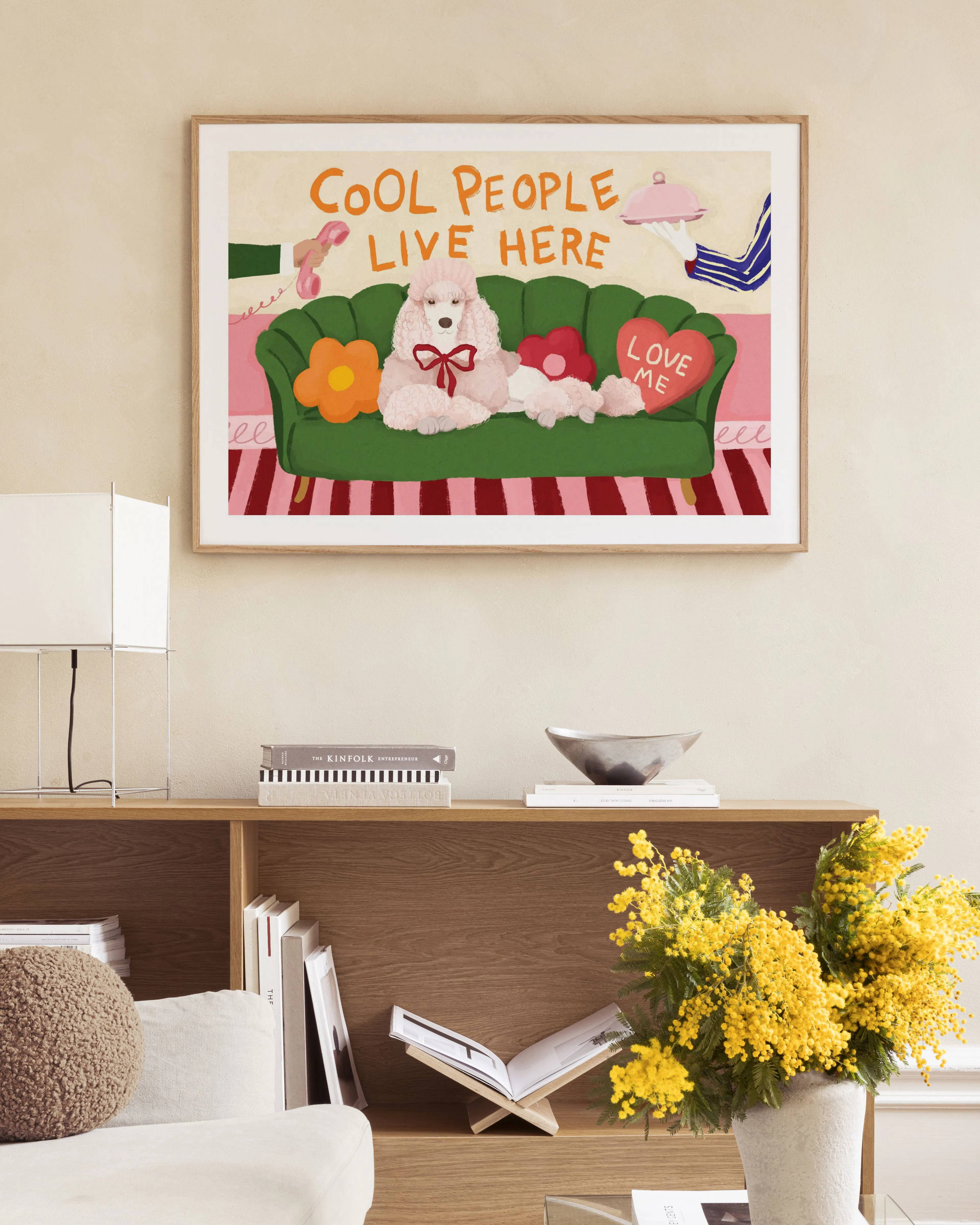 Poster con barboncino rosa su divano verde, cuori e scritta Cool People Live Here, appeso in un soggiorno moderno.