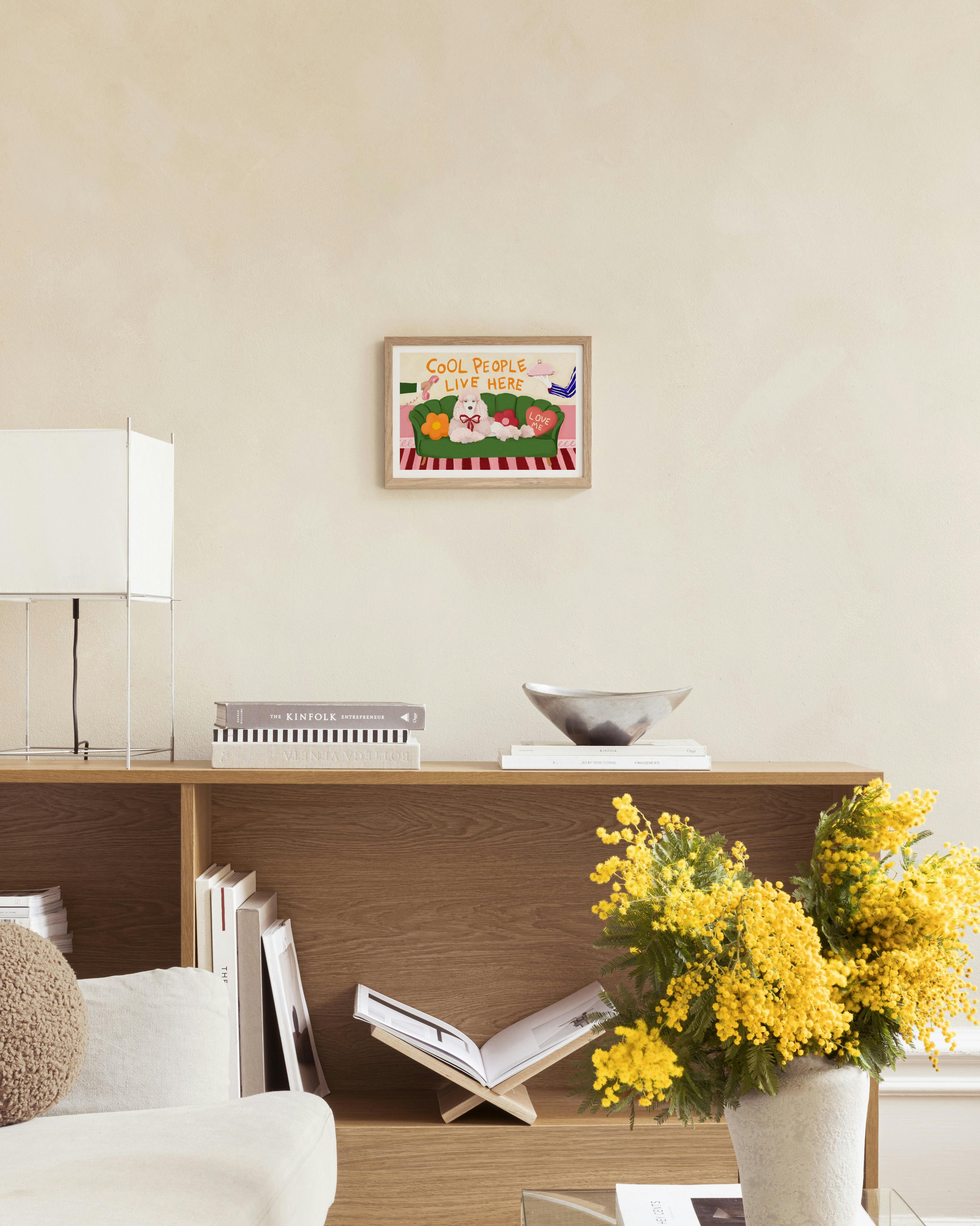 A colorful print of a white poodle on a green couch with pink and orange pillows, text COOL PEOPLE LIVE HERE, hung in a cozy liv