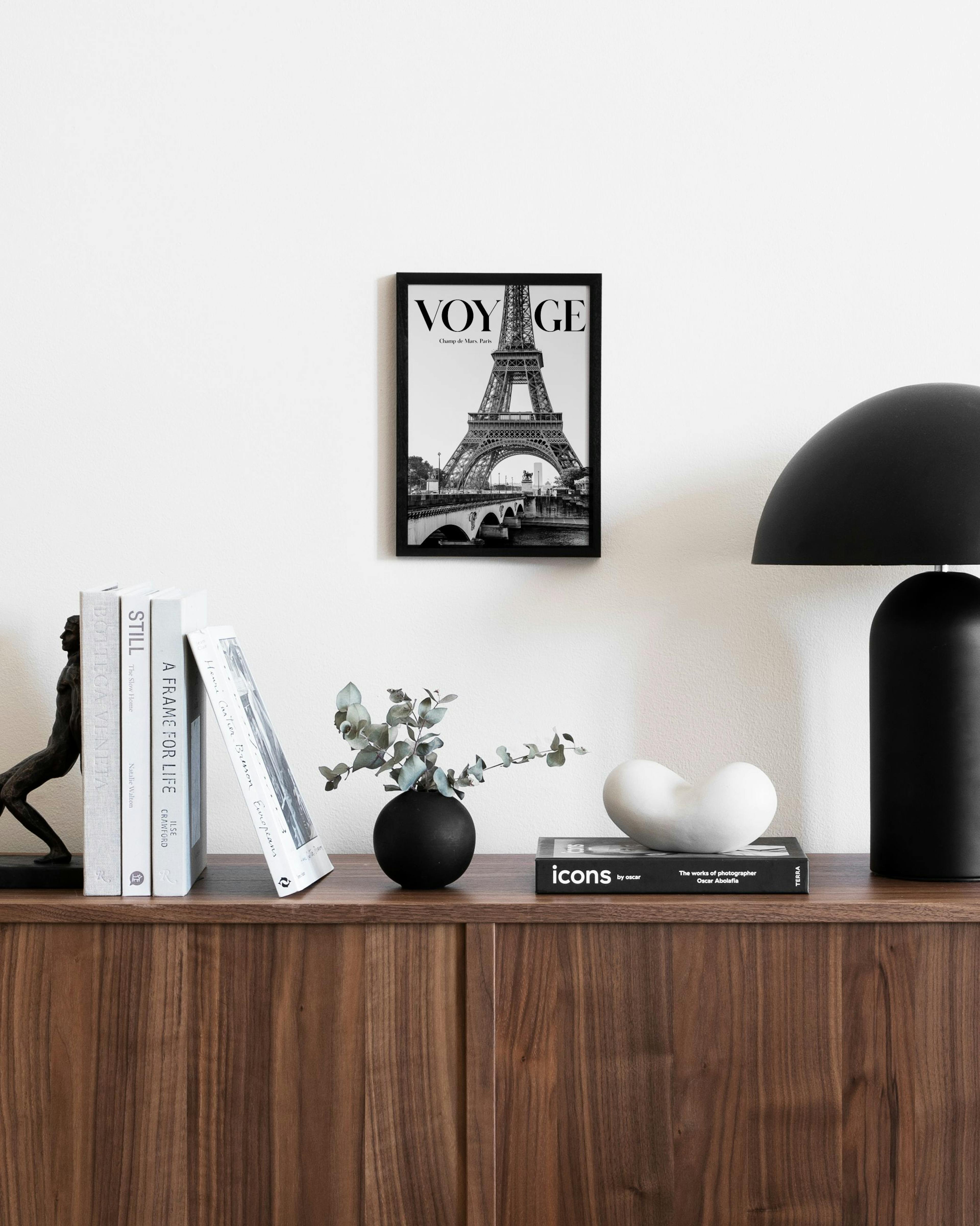 Μονόχρωμη αφίσα με τον Πύργο του Άιφελ και τη λέξη VOYAGE, κρεμασμένη πάνω από ένα ξύλινο μπουφέ σε μοντέρνο σαλόνι.