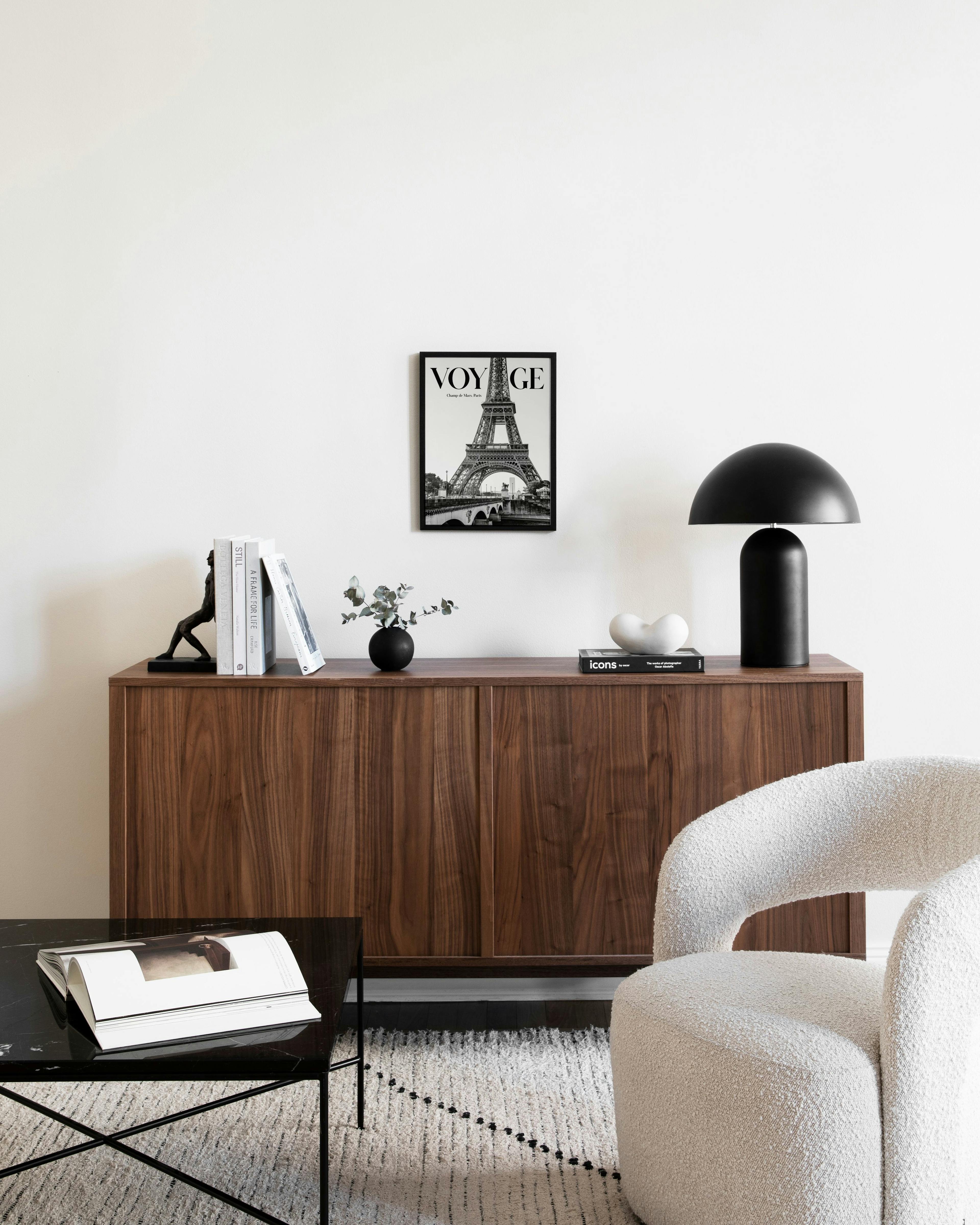 Affiche noir et blanc de la Tour Eiffel avec le mot VOYAGE, accrochée au-dessus dun buffet en bois.