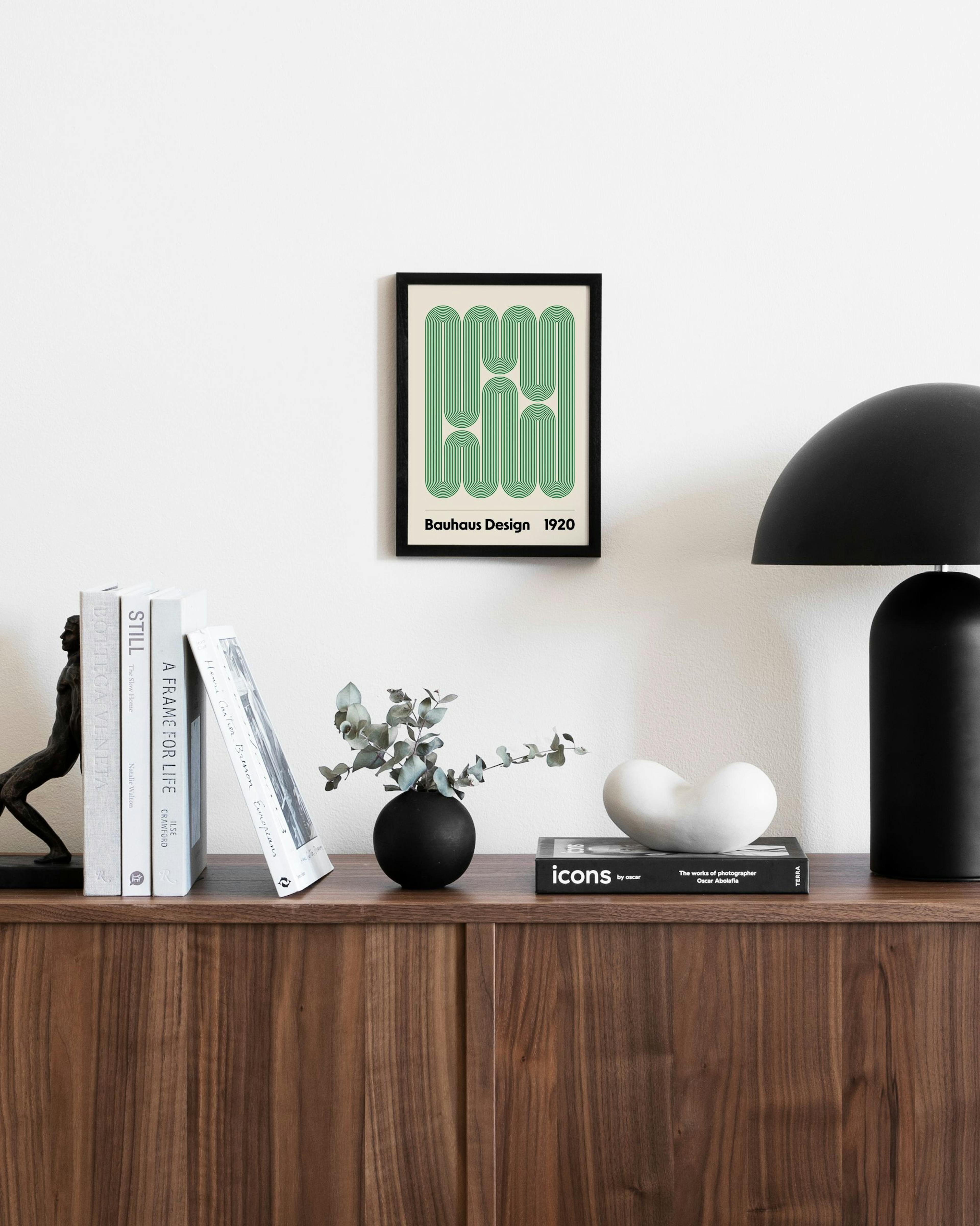 따뜻한 베이지색 배경에 녹색 선이 기하학적 패턴을 이루는 바우하우스 디자인 포스터가 갈색 수납장 위에 걸려 있습니다.