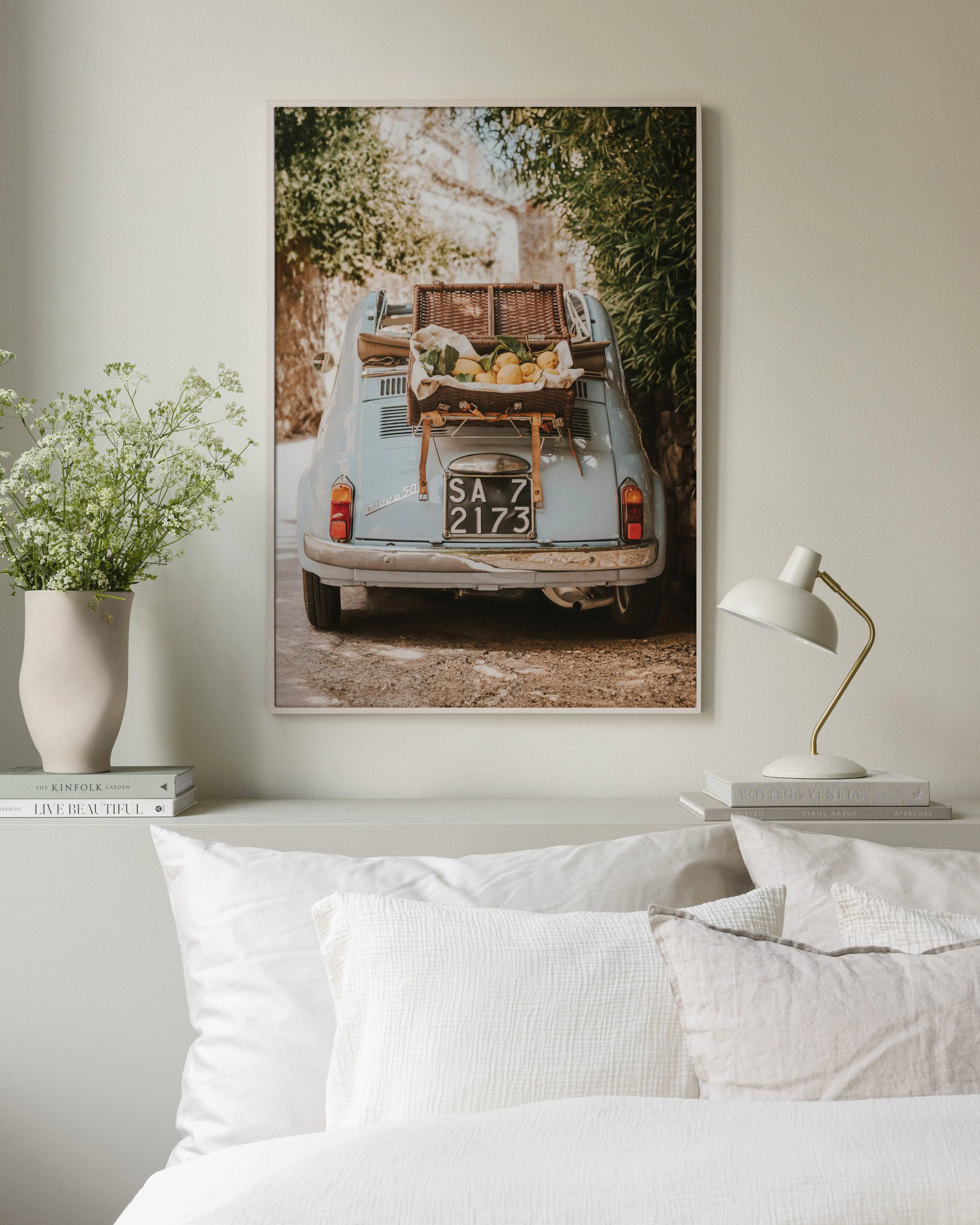 Poster van een lichtblauwe oldtimer met picknickmand en citroenen op de achterklep, hangend boven een bed.