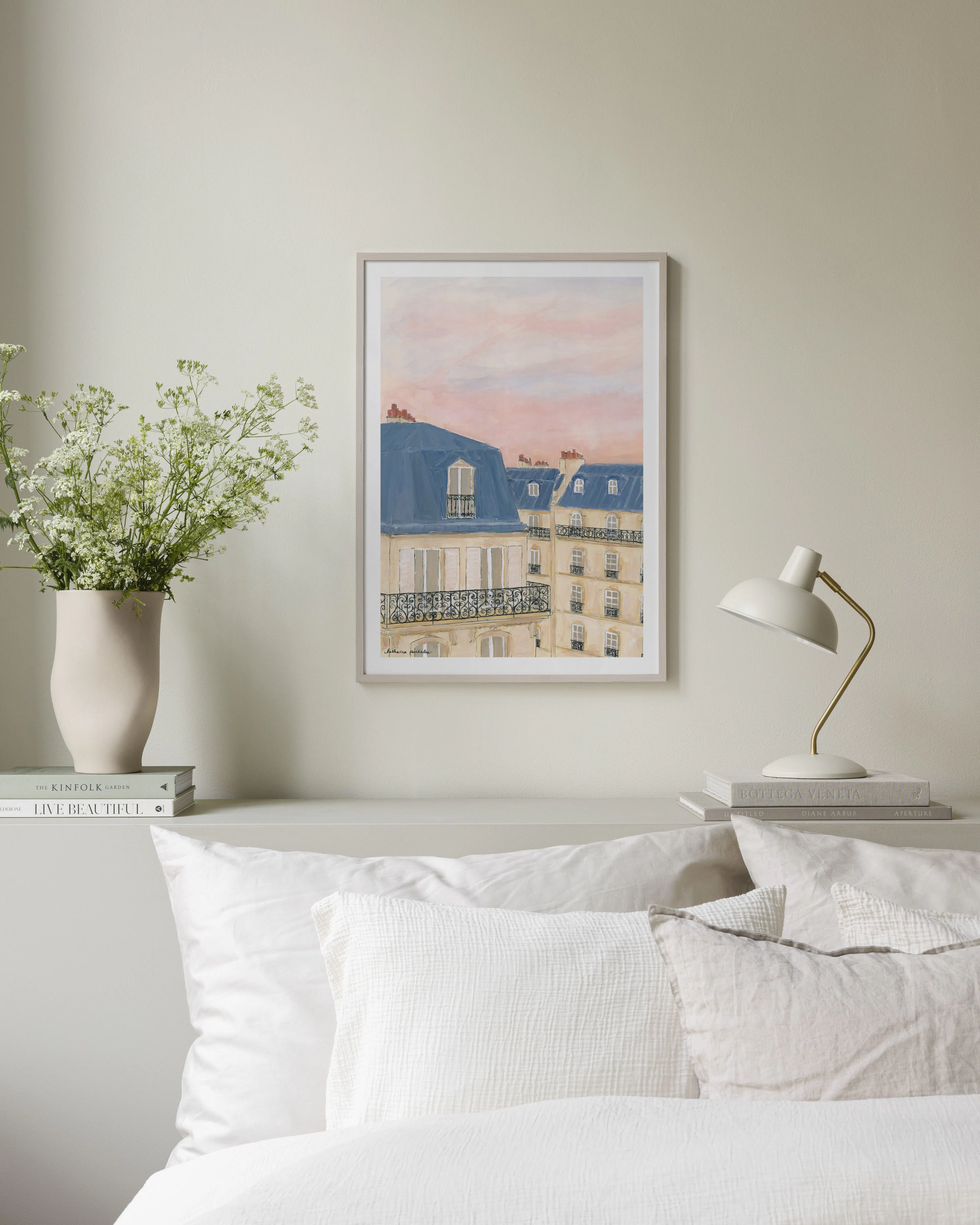 Poster med akvarellmålning av parisiska byggnader med blå tak och balkonger, hängande över en ljus soffa i ett vardagsrum.