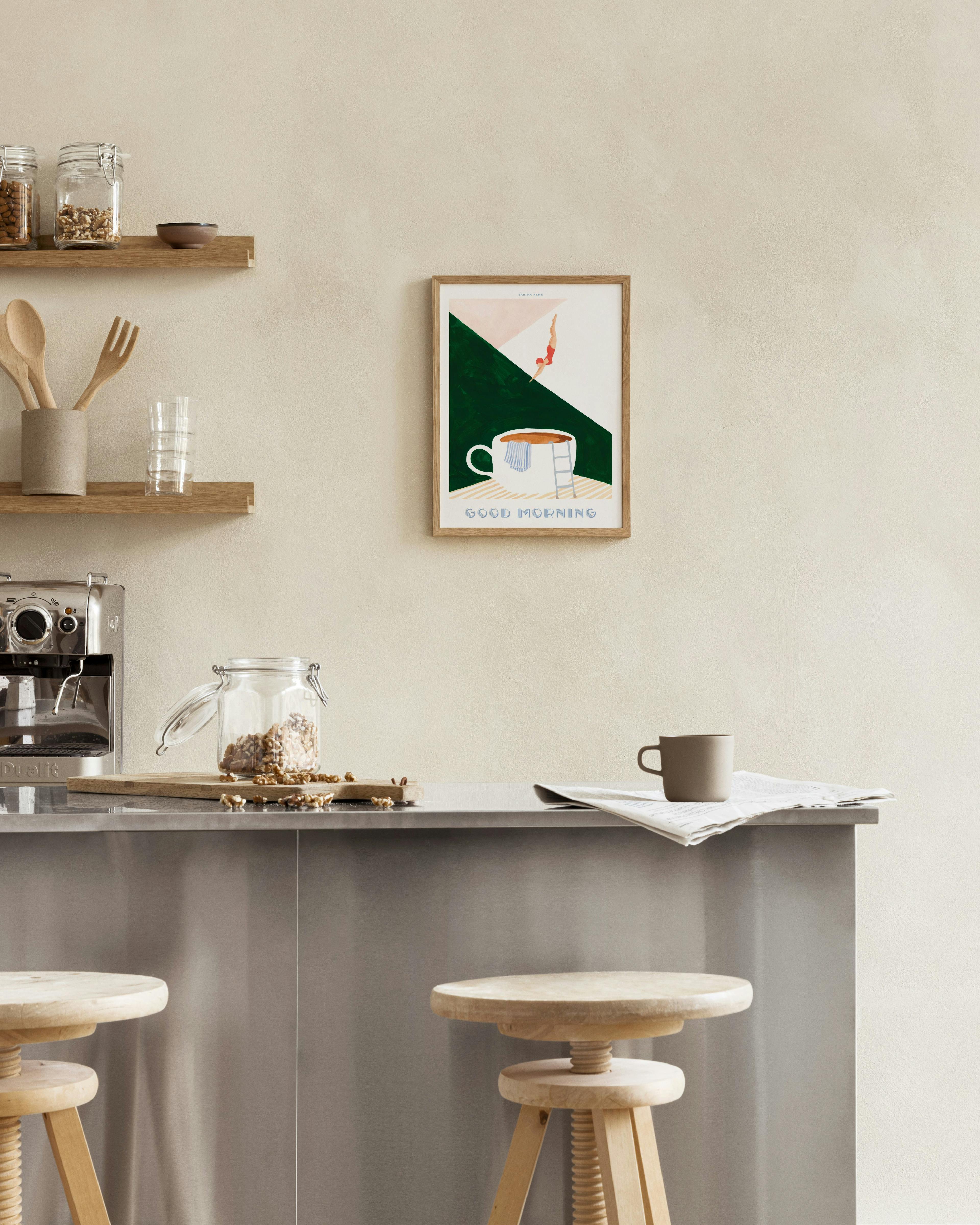 Poster mit Taucherin, die in eine große Kaffeetasse springt, darüber Good Morning“, hängt über einem Holztisch mit Croissant und