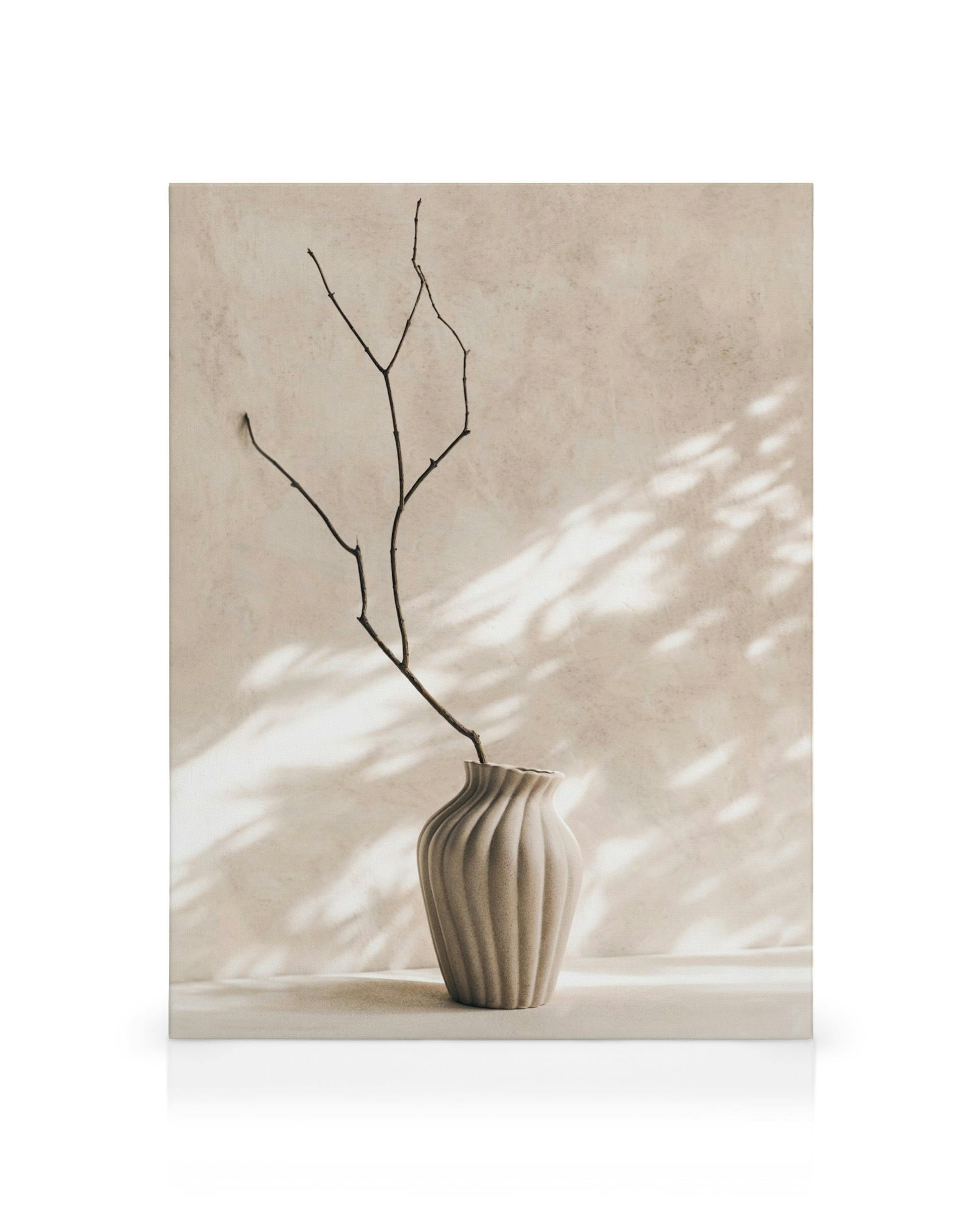Leinwandbild mit einer beigen gerillten Vase, aus der ein kahler Ast ragt, vor einer beigen Wand mit Sonnenlicht.