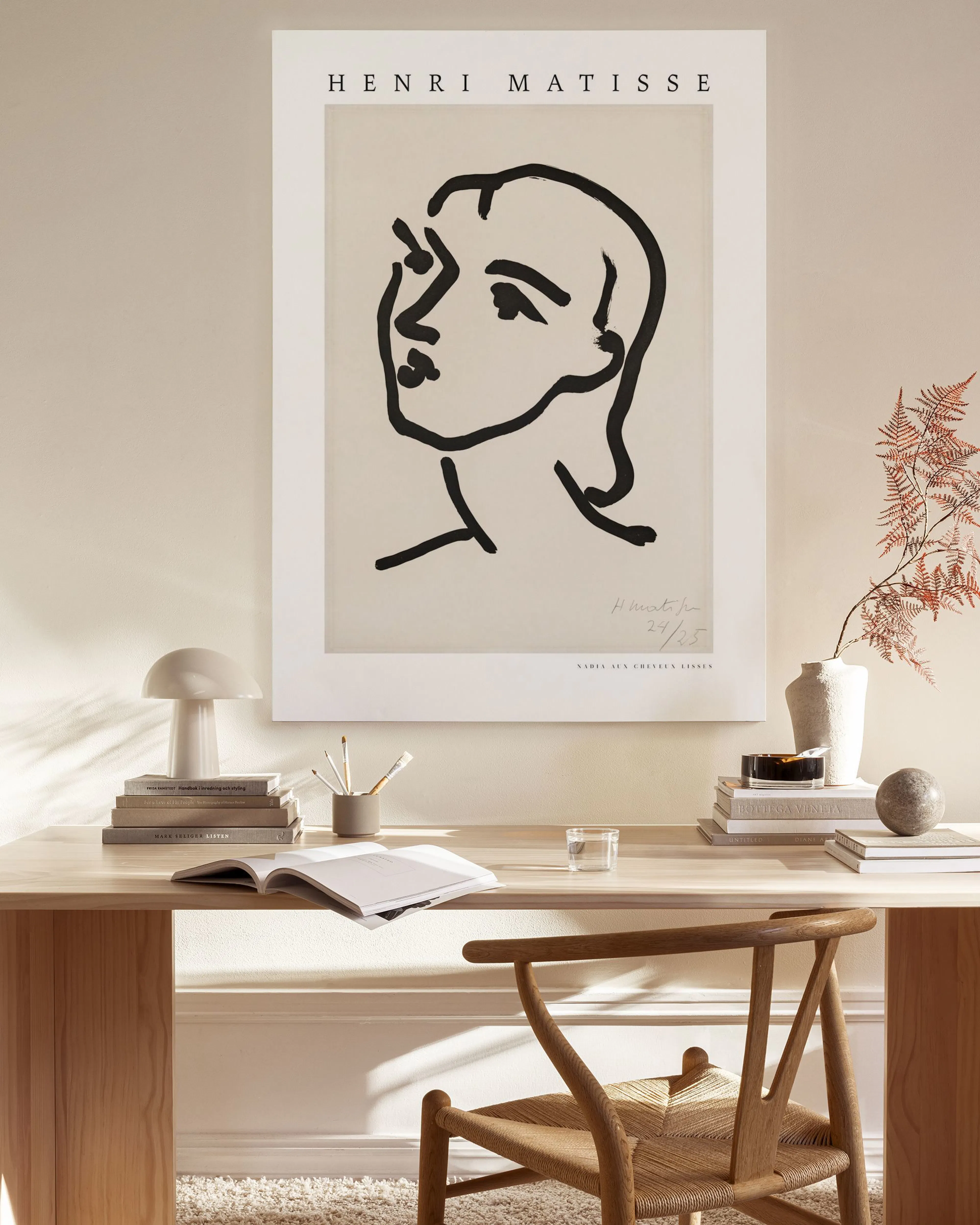 Obraz na plátne s minimalistickou čiernou kresbou tváre Henriho Matisse visí v modernom interiéri nad drevenou komodou.