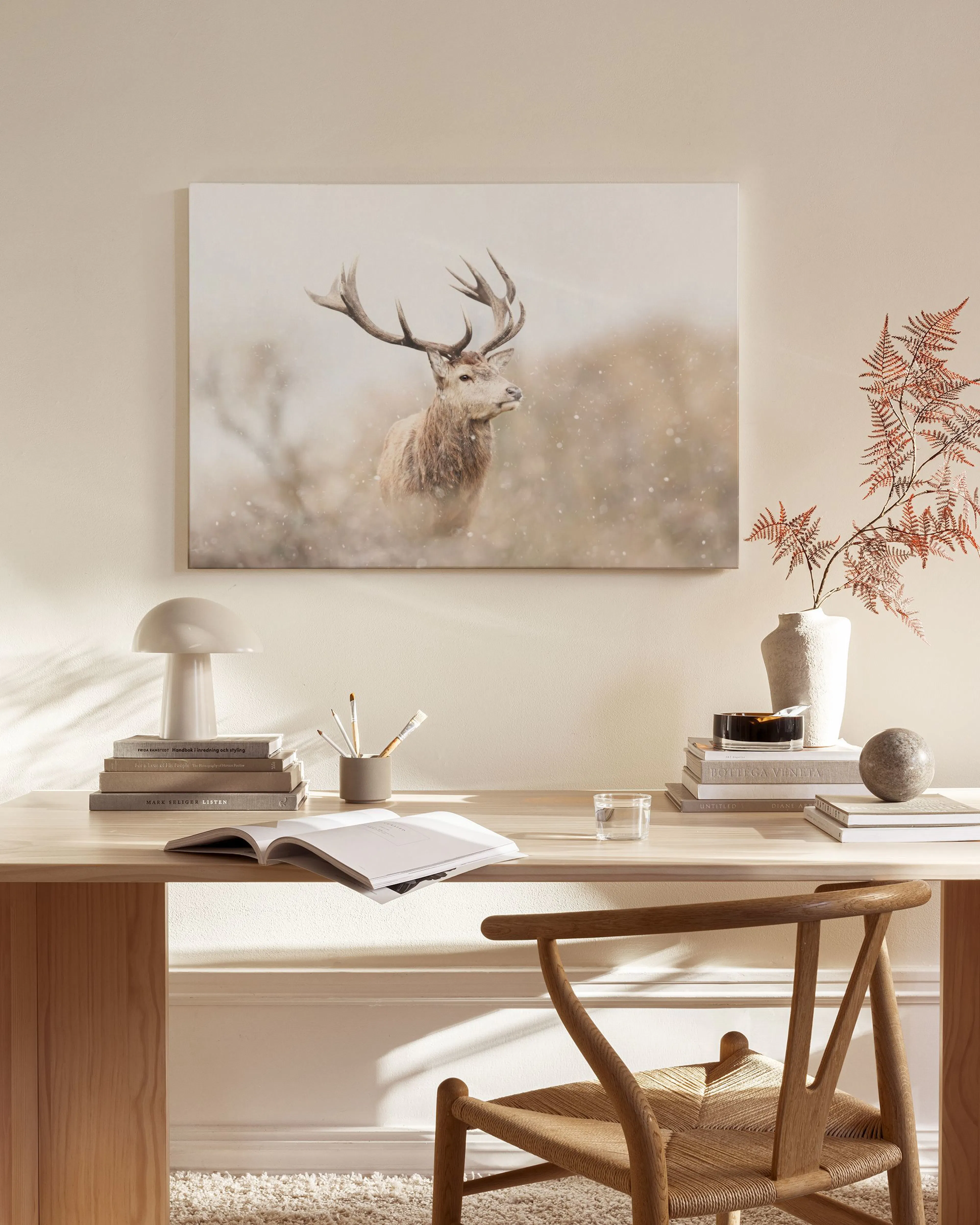 Toile dun cerf avec de grands bois, debout dans un champ enneigé, accrochée dans un salon scandinave.