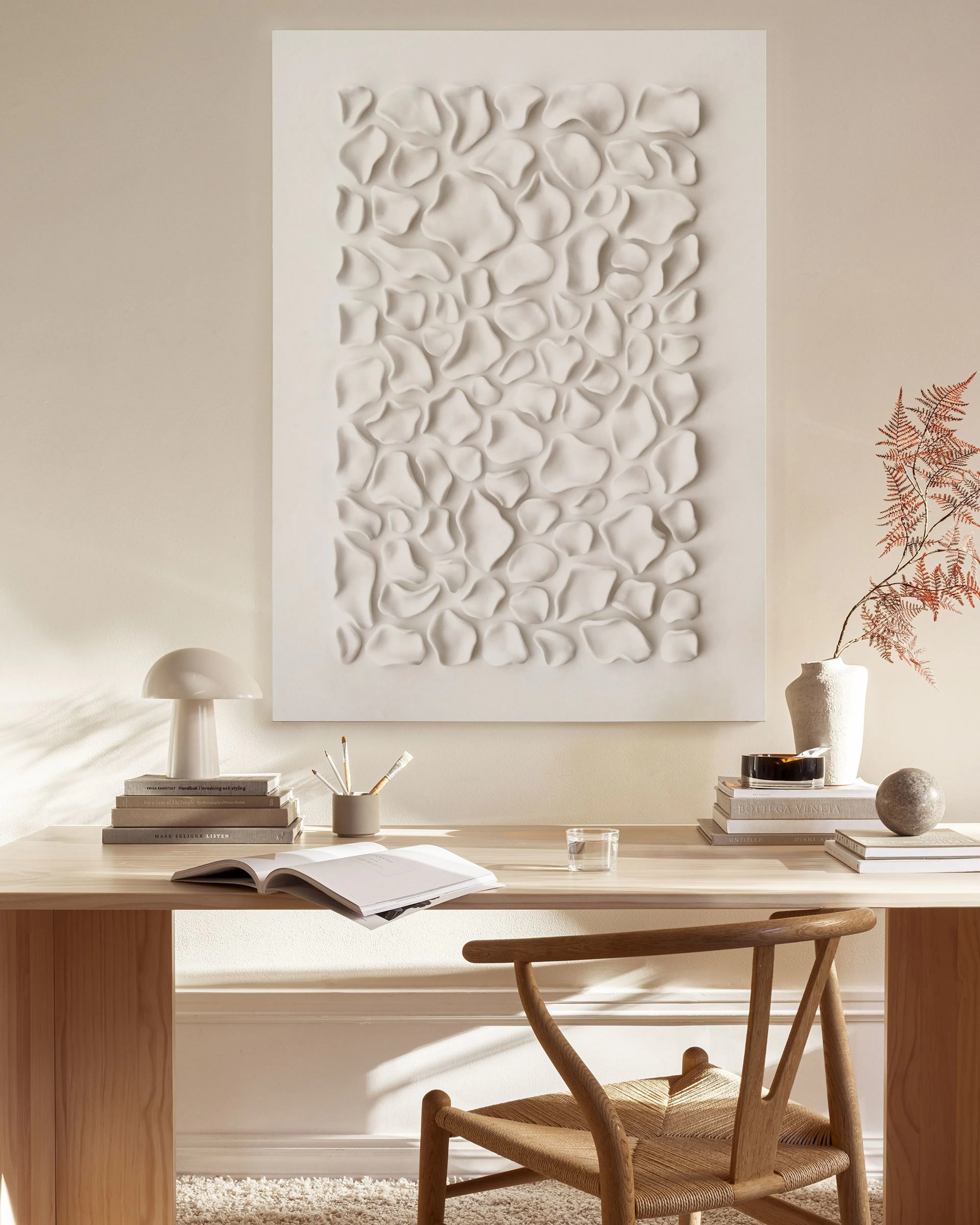 A white abstract relief art piece with organic shapes, hanging above a wooden console table in a minimalist living room.