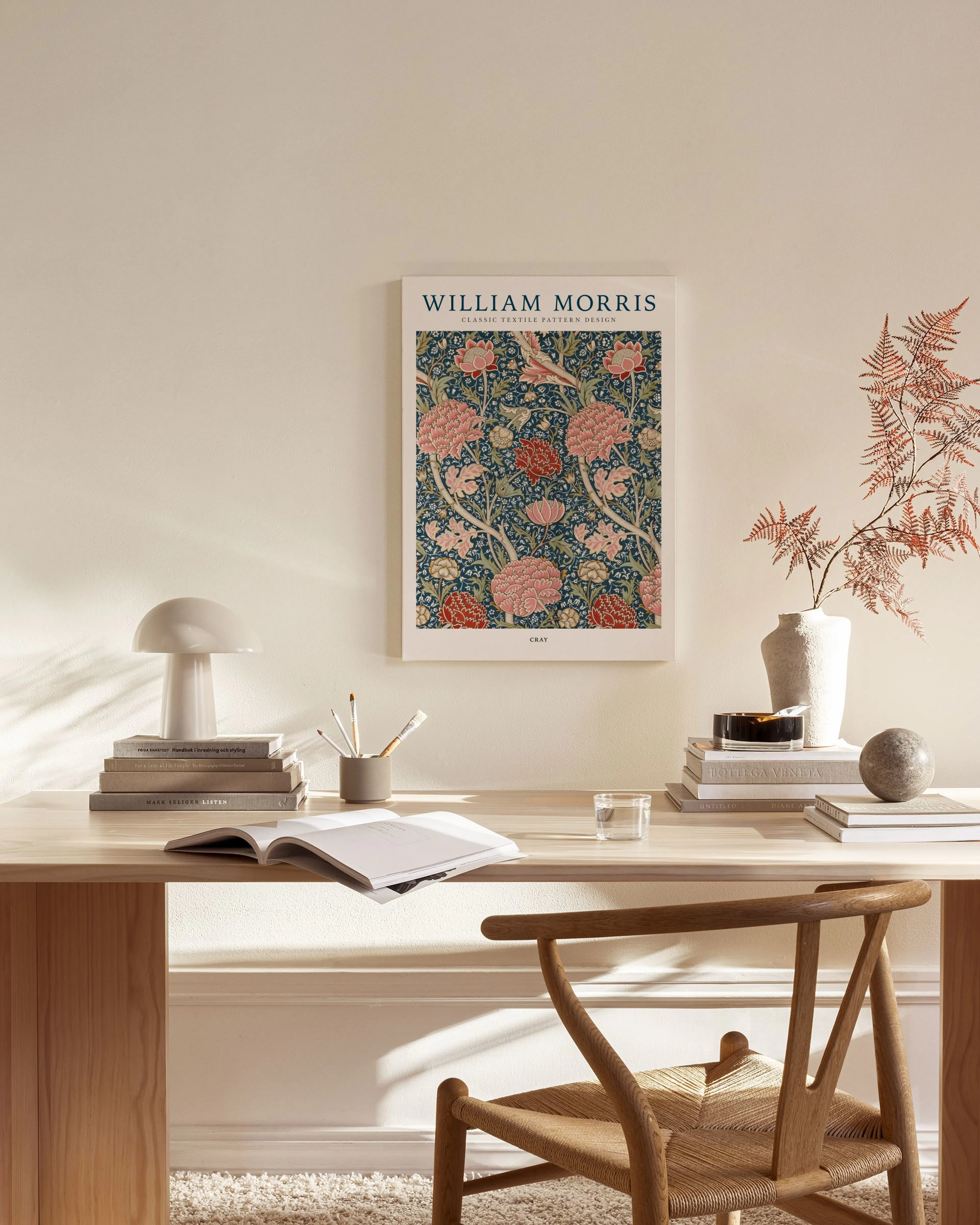 Et William Morris lerretsbilde med blomstermotiv i rosa og rødt på mørk bunn, henger i en lys stue.
