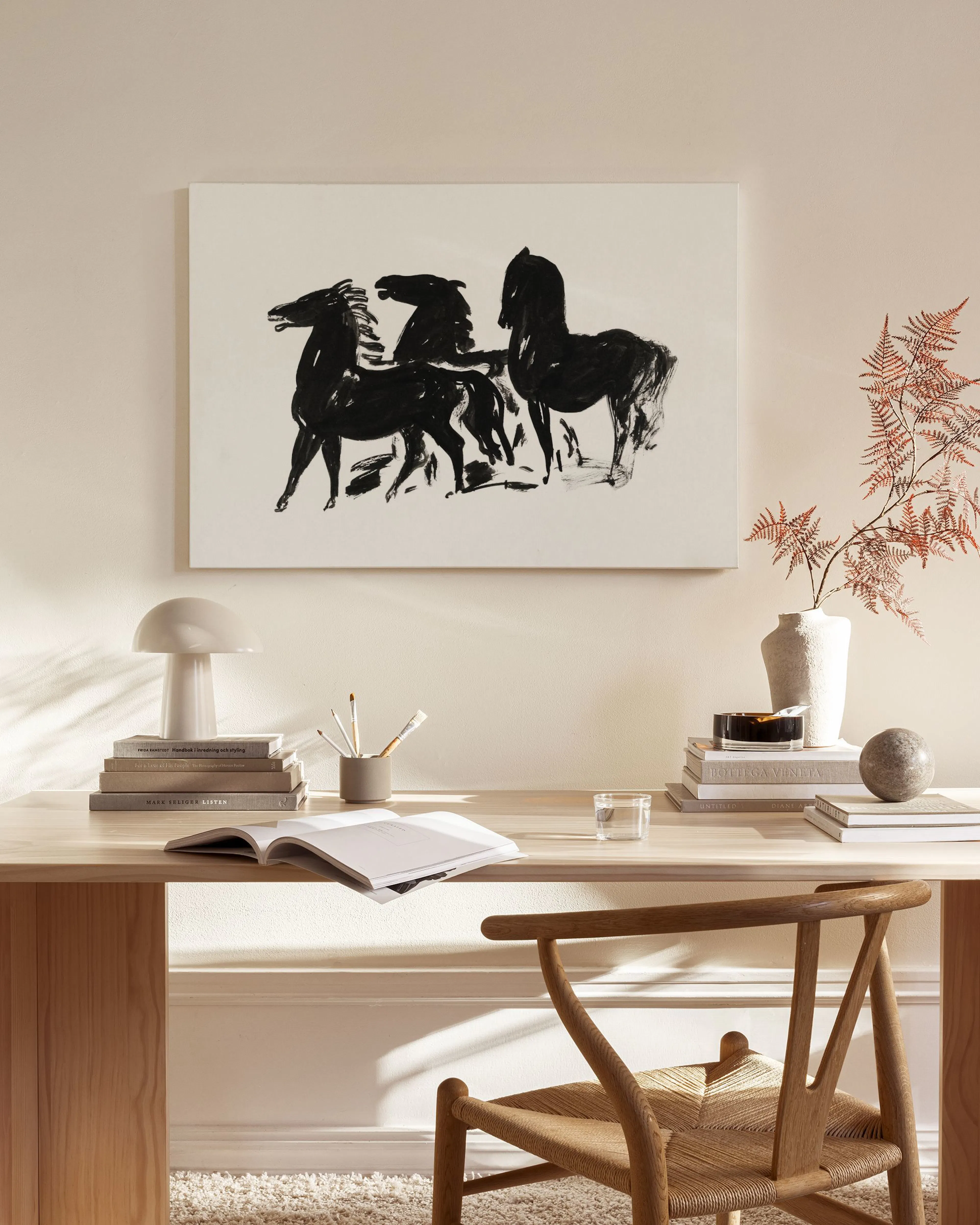 A black and white canvas print depicting horses, displayed above a wooden console table in a minimalist living room.