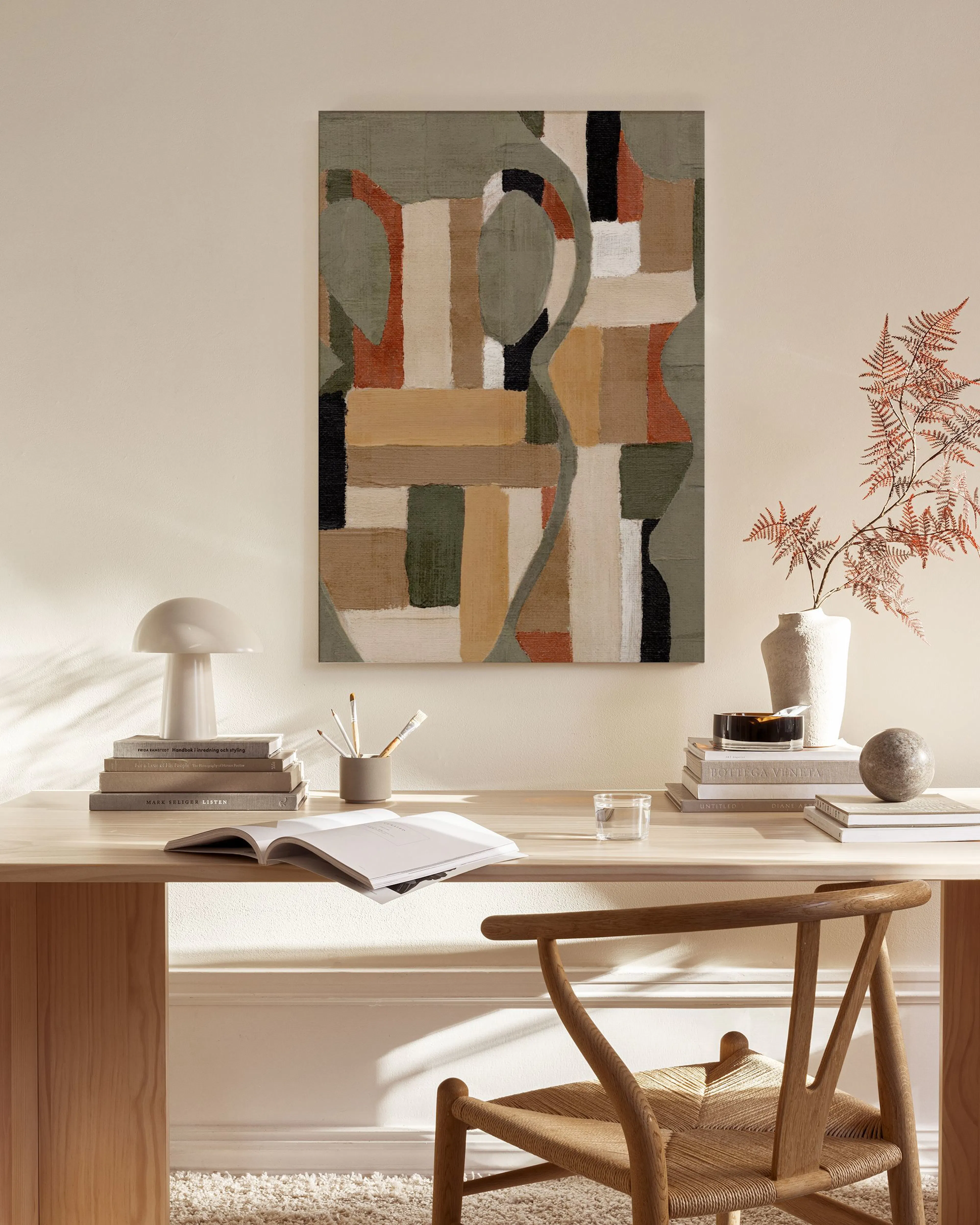 Leinwandbild mit abstrakten Formen in Beige, Grün und Rostrot, hängt über einem Holzregal in einem Wohnzimmer.