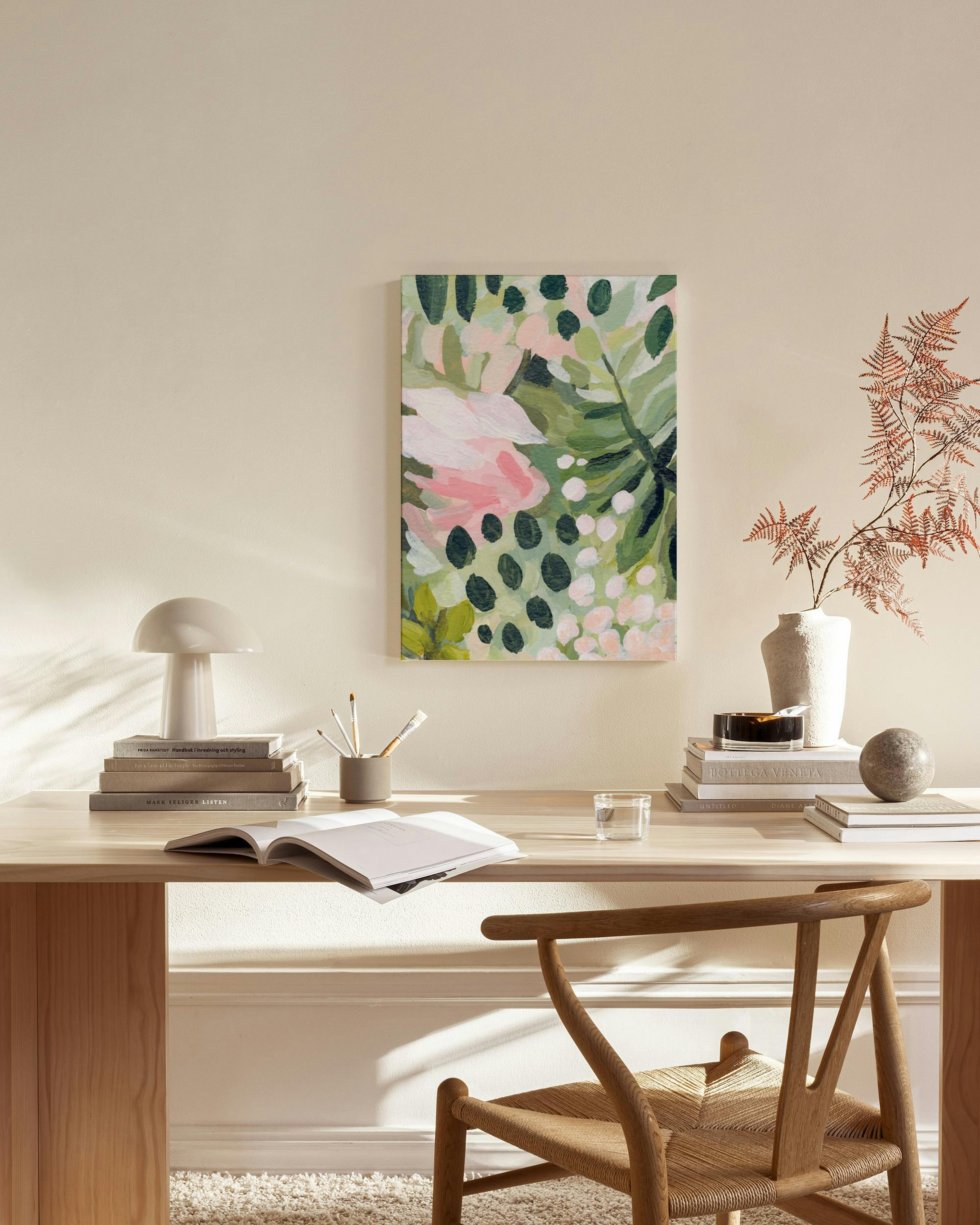 Canvastavla med grönskande löv och rosa blommor på en beige vägg ovanför en träbänk i ett vardagsrum.