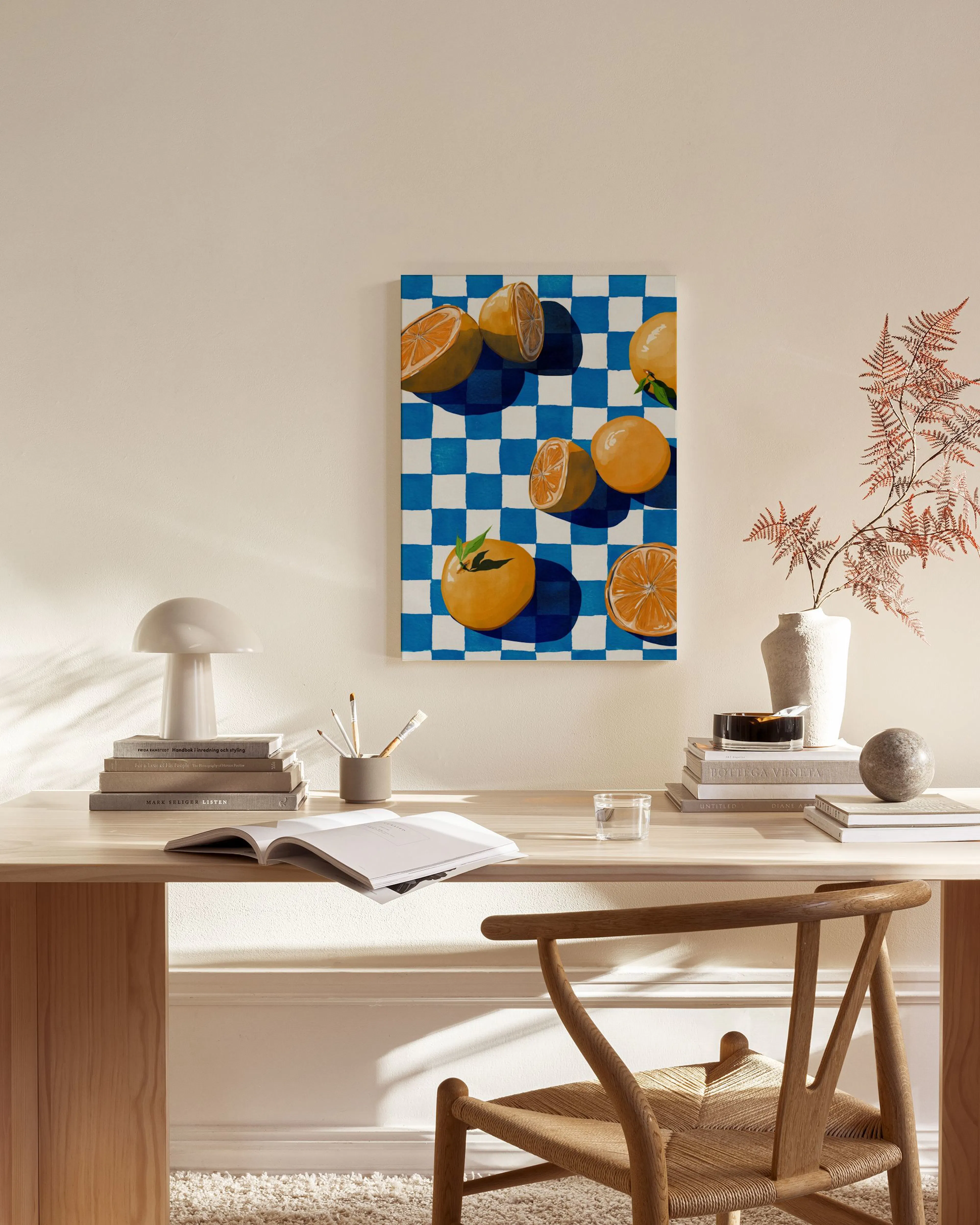 Toile de fruits oranges sur un motif à carreaux bleus et blancs, accrochée au mur dun salon moderne avec fauteuil en bois, table