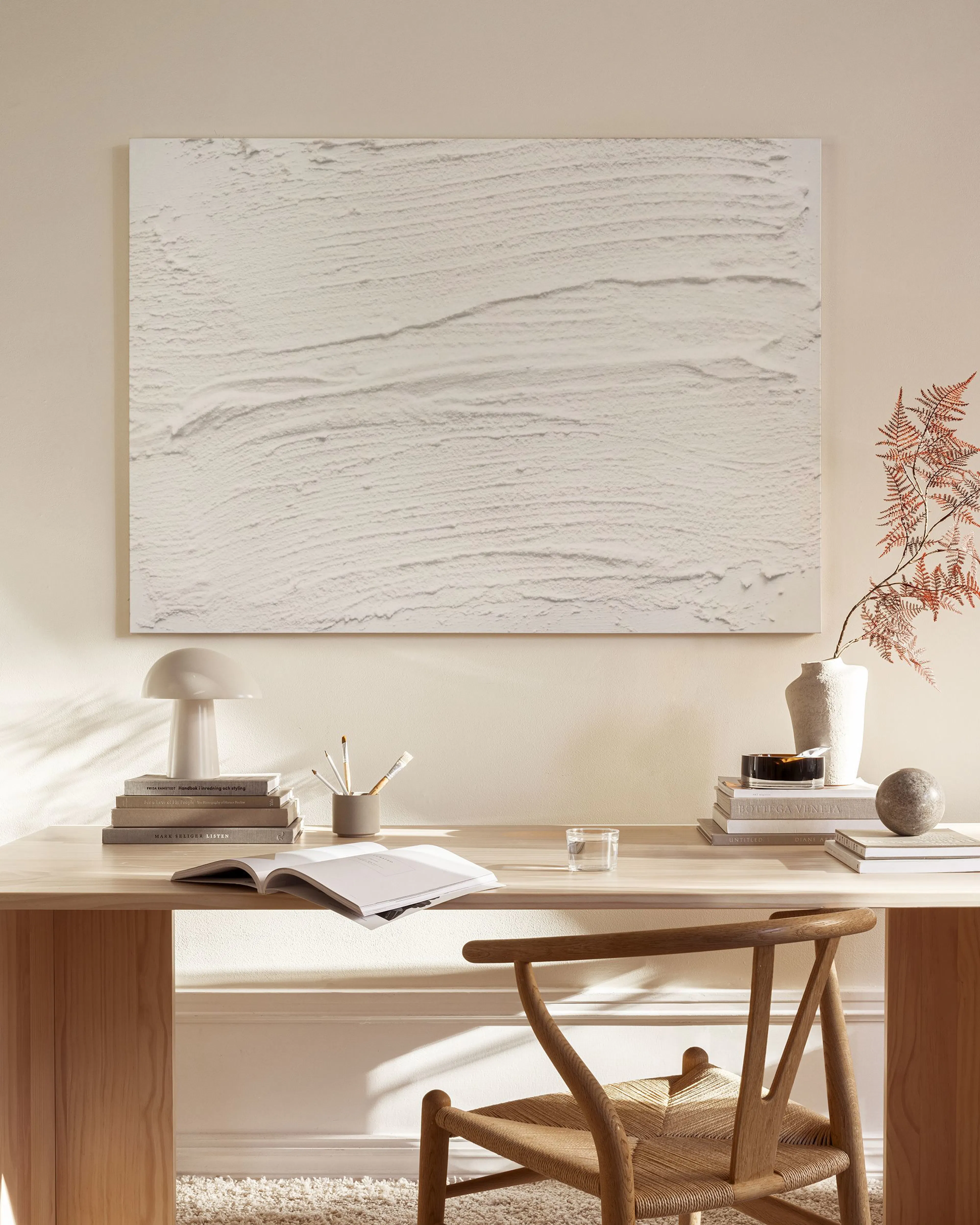 Toile texturée blanche aux motifs abstraits, suspendue au-dessus dun meuble bas en bois dans un salon moderne.