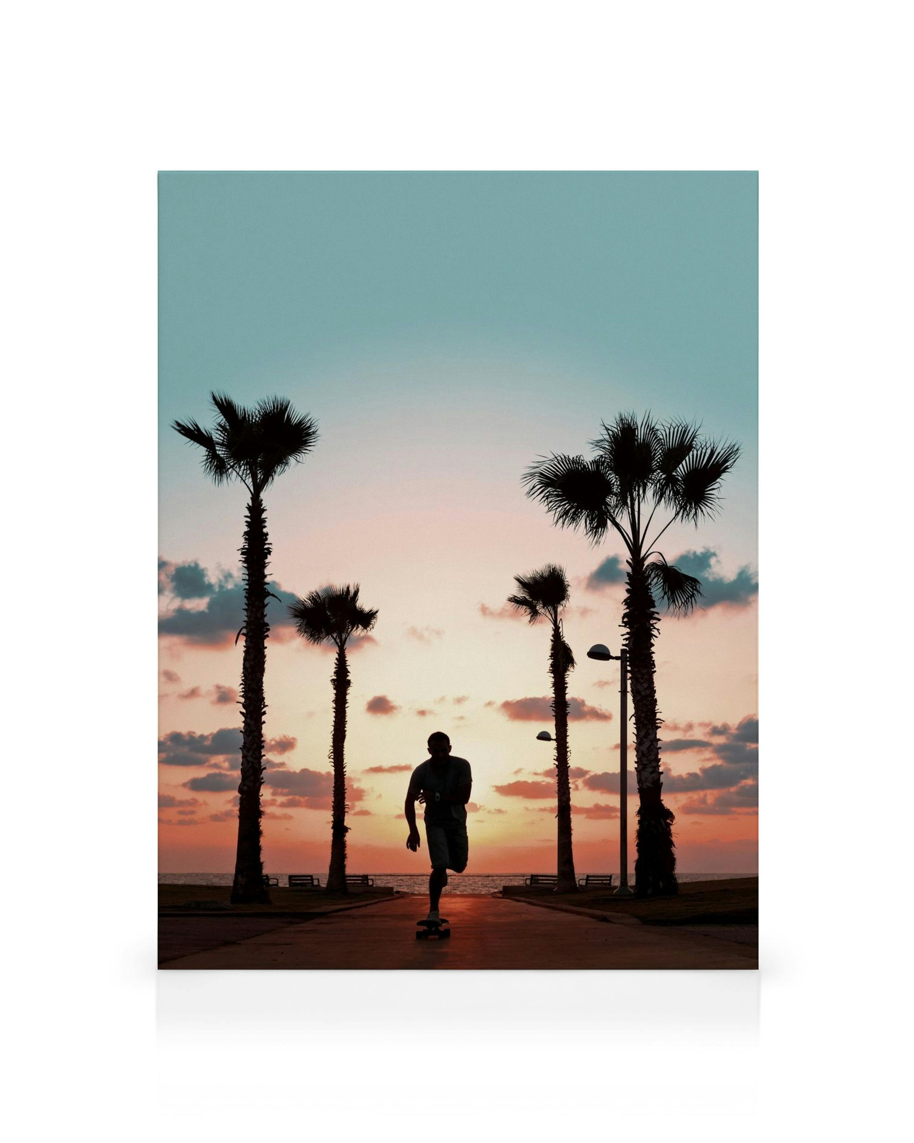 Auringonlaskun kanvaasi, jossa skeittaaja liukuu palmupuiden reunustamalla rantakadulla.
