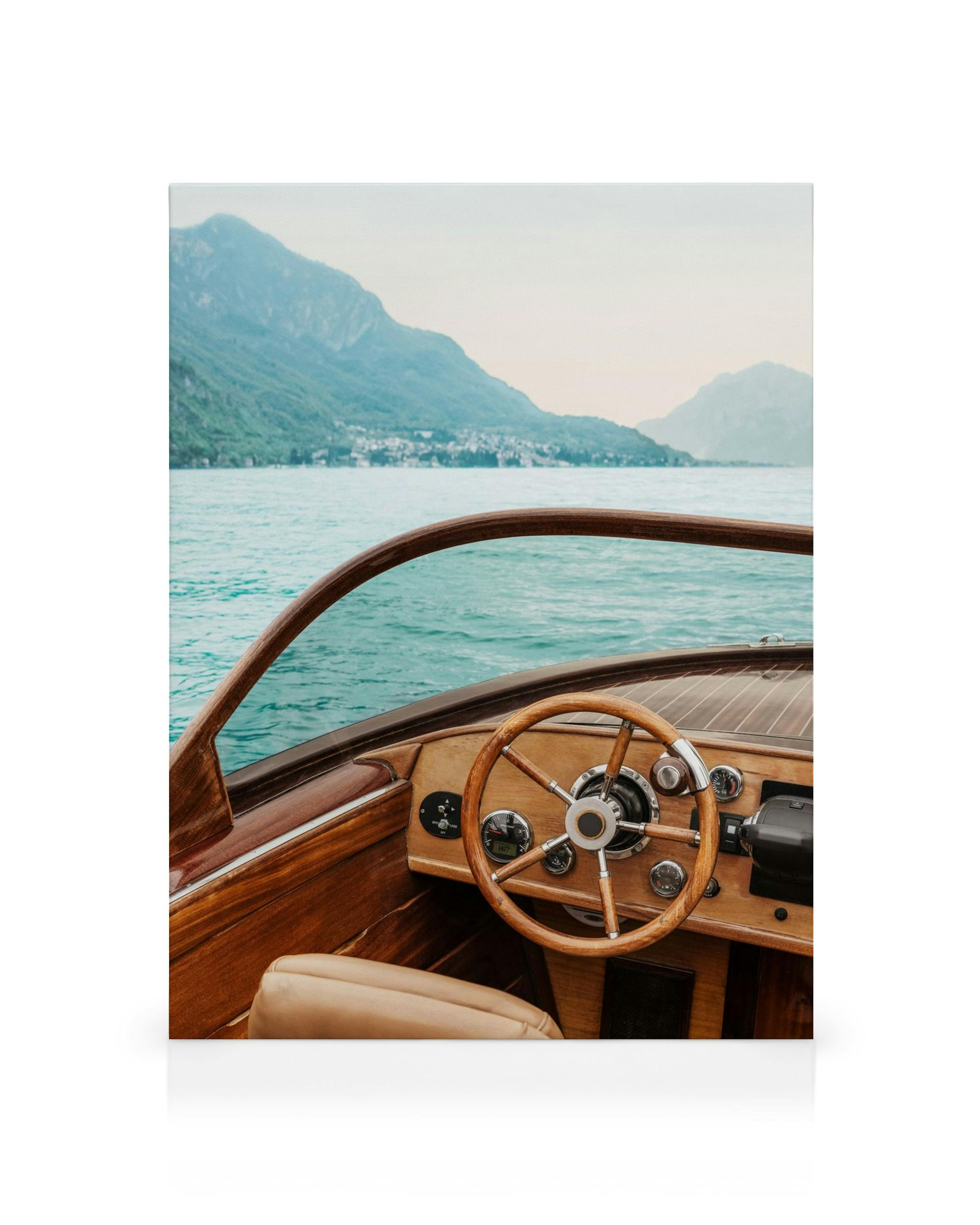 Wooden boat interior with steering wheel, blue lake, and green mountains under a pale sky, serene moment.